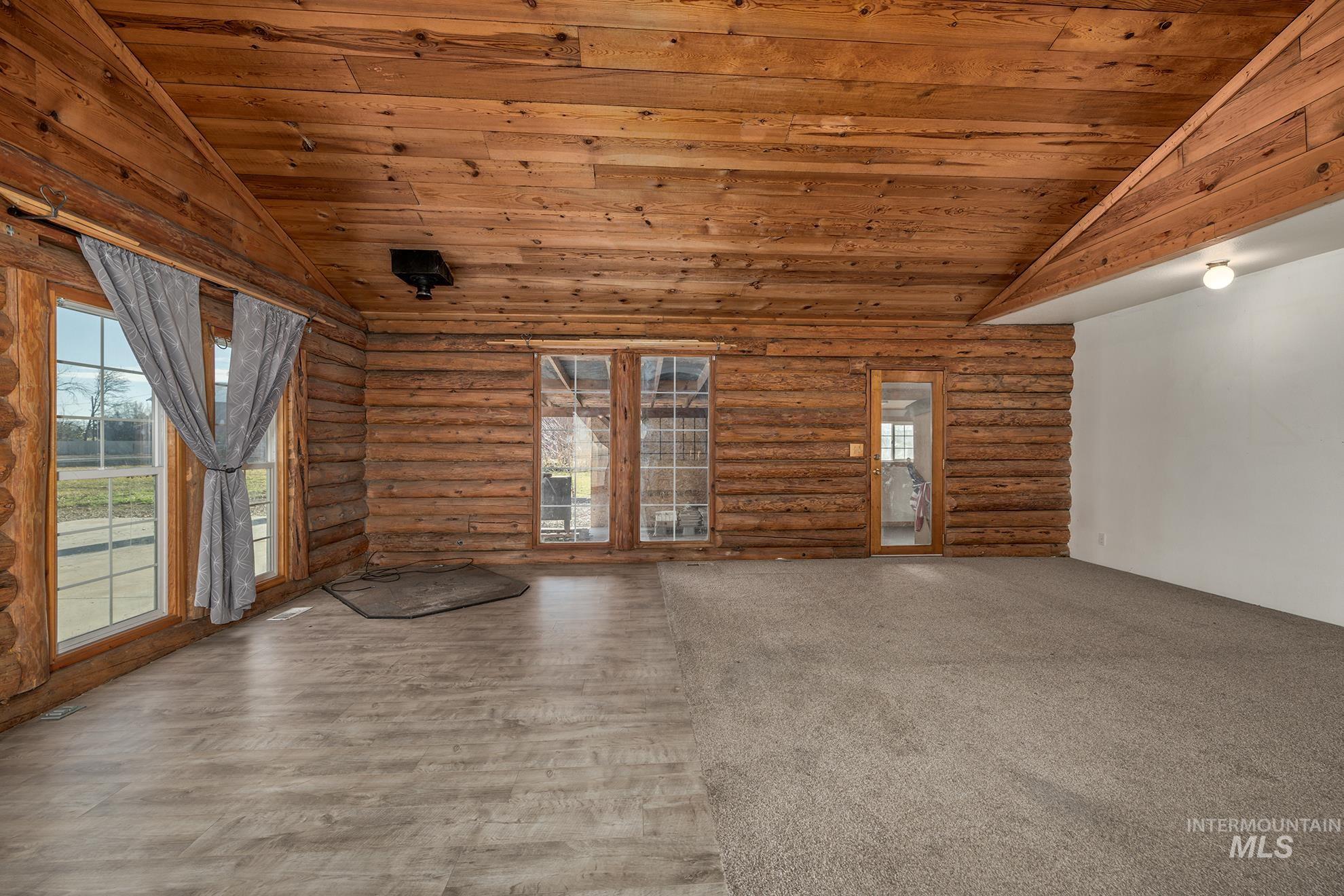 Unfurnished living room featuring wooden ceiling, lofted ceiling, log walls, and light wood-style floors