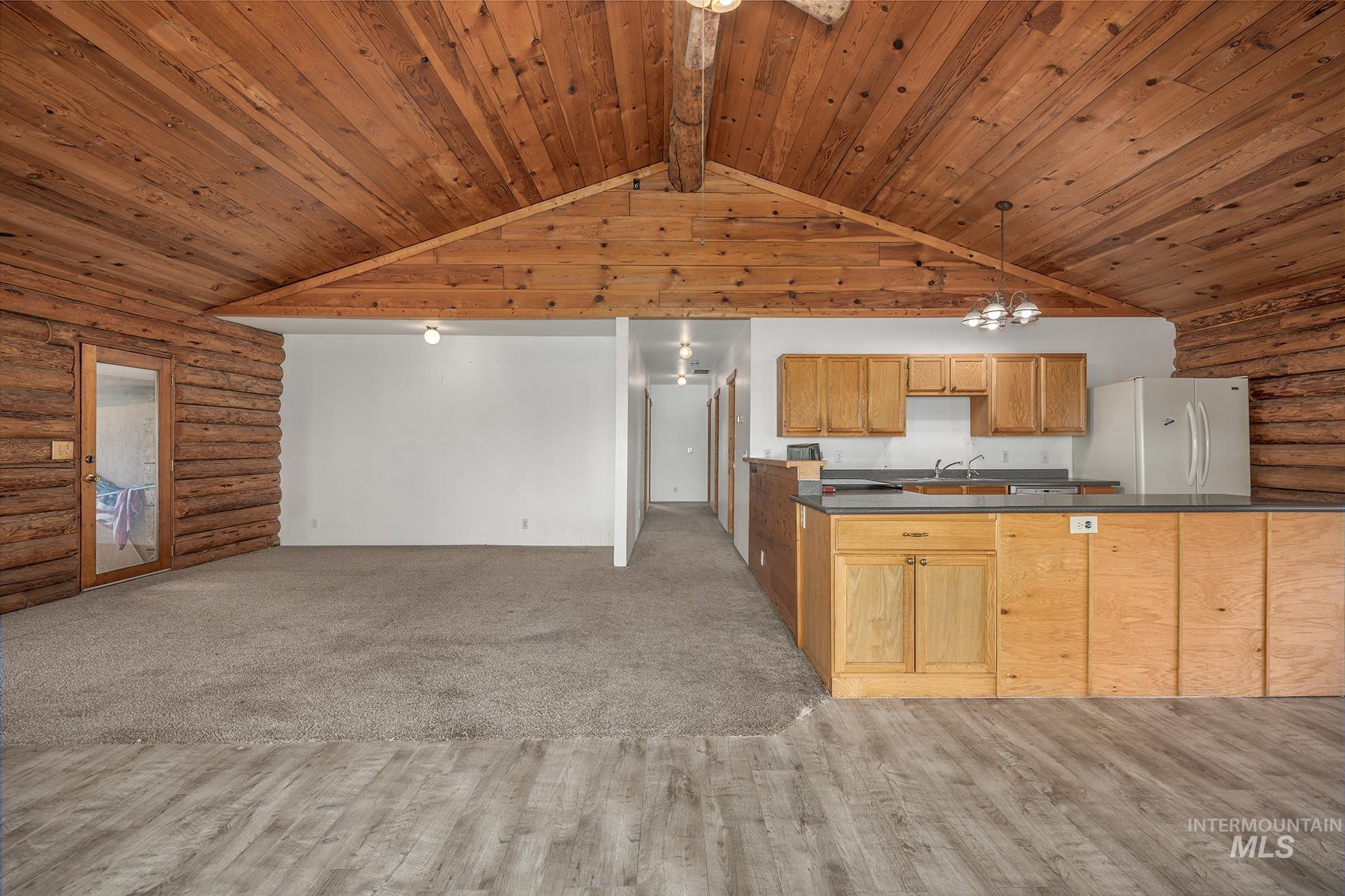Kitchen featuring rustic walls, dark countertops, open floor plan, pendant lighting, and wood ceiling