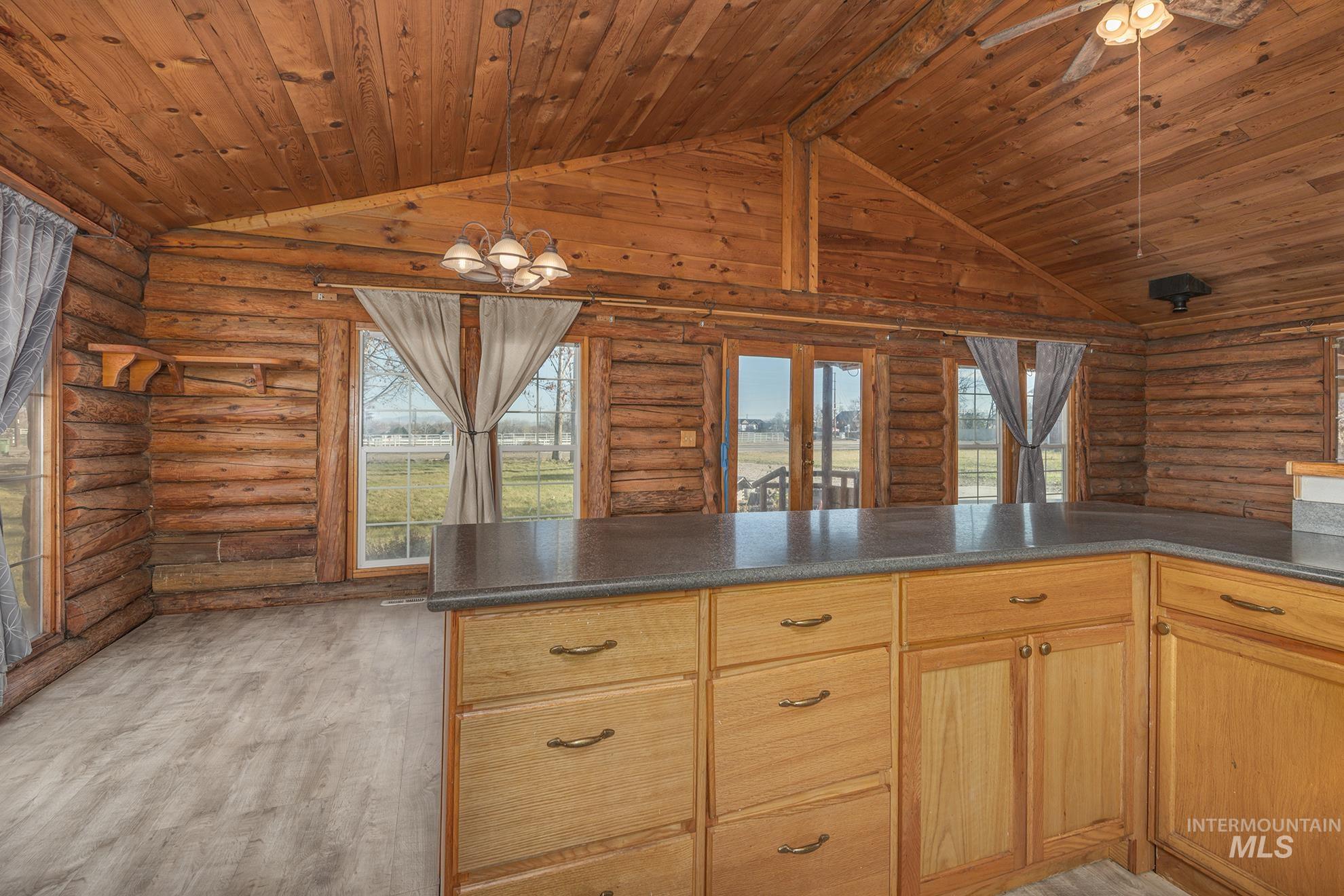 Kitchen featuring light wood finished floors, dark countertops, pendant lighting, vaulted ceiling, and wooden ceiling