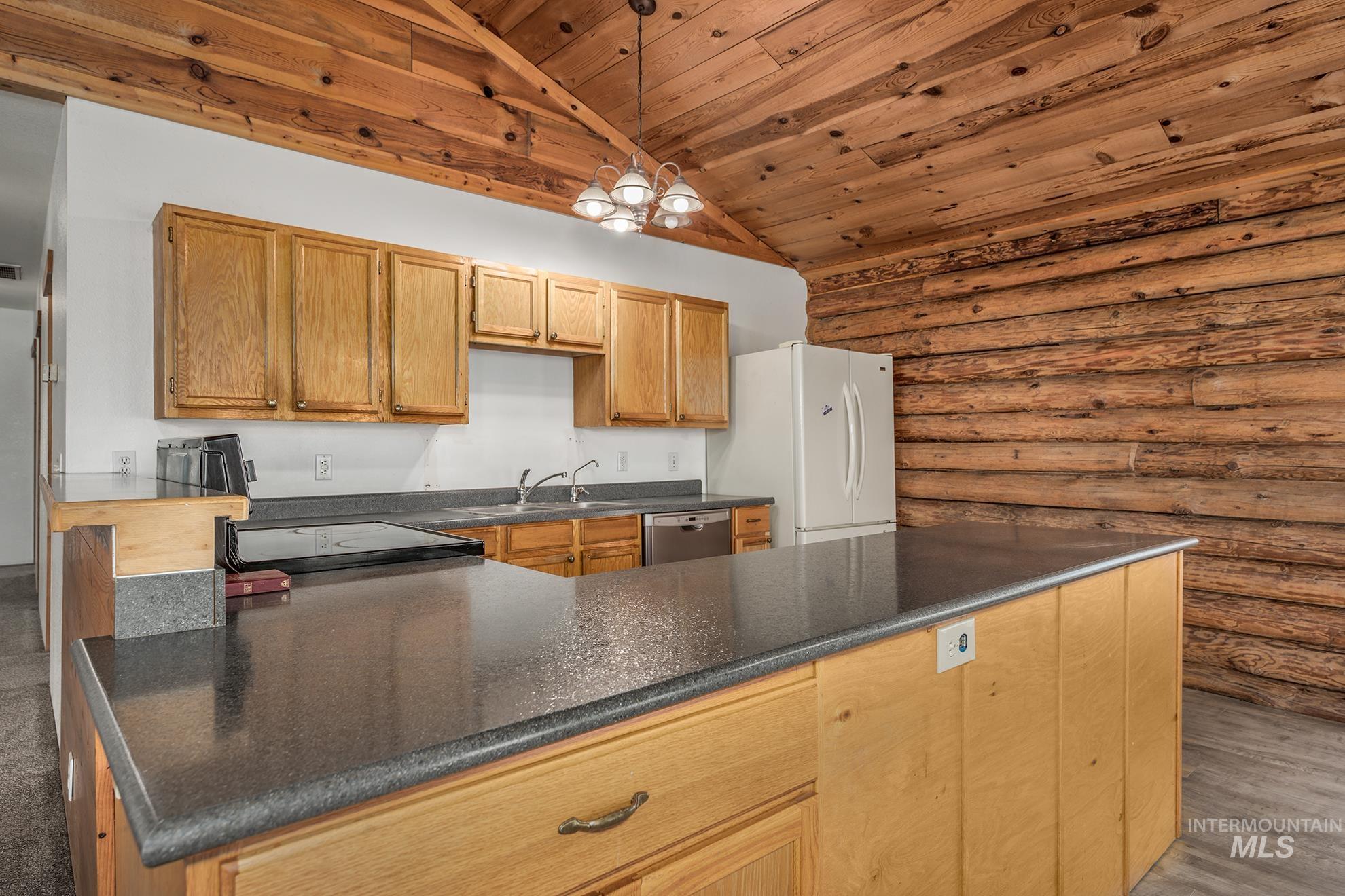 Kitchen featuring rustic walls, pendant lighting, wooden ceiling, a peninsula, and vaulted ceiling