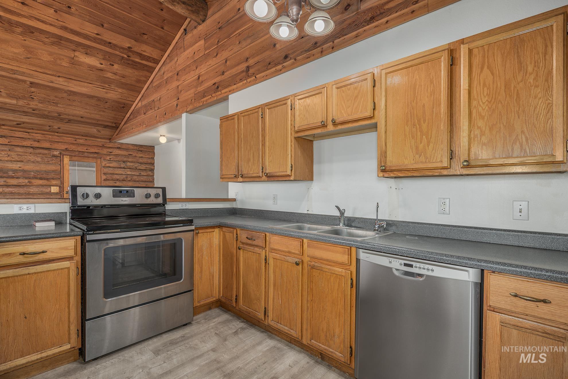Kitchen with stainless steel appliances, dark countertops, light wood finished floors, wood ceiling, and log walls