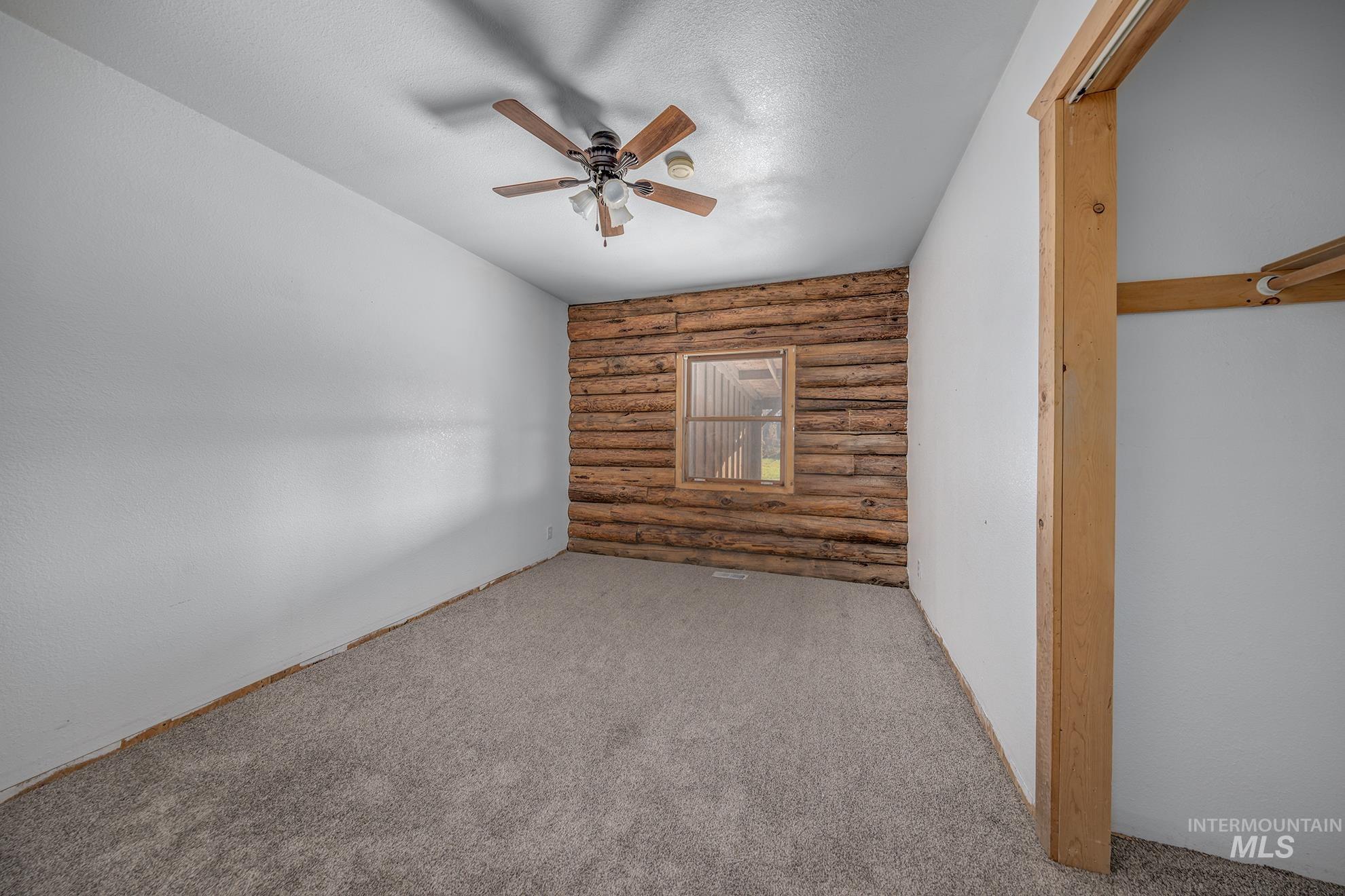 Carpeted spare room featuring rustic walls, a ceiling fan, and a textured ceiling