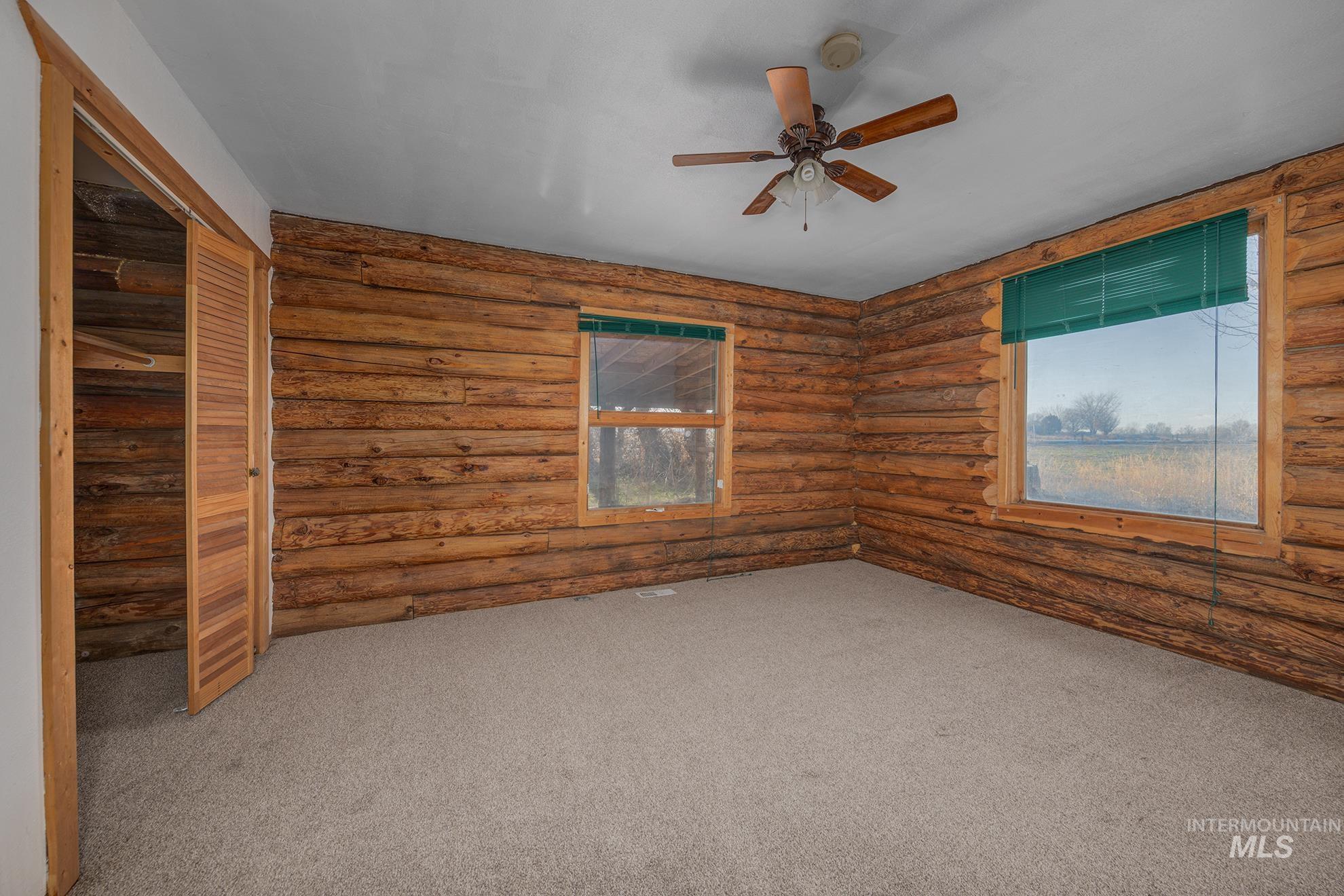 Carpeted empty room with log walls and a ceiling fan