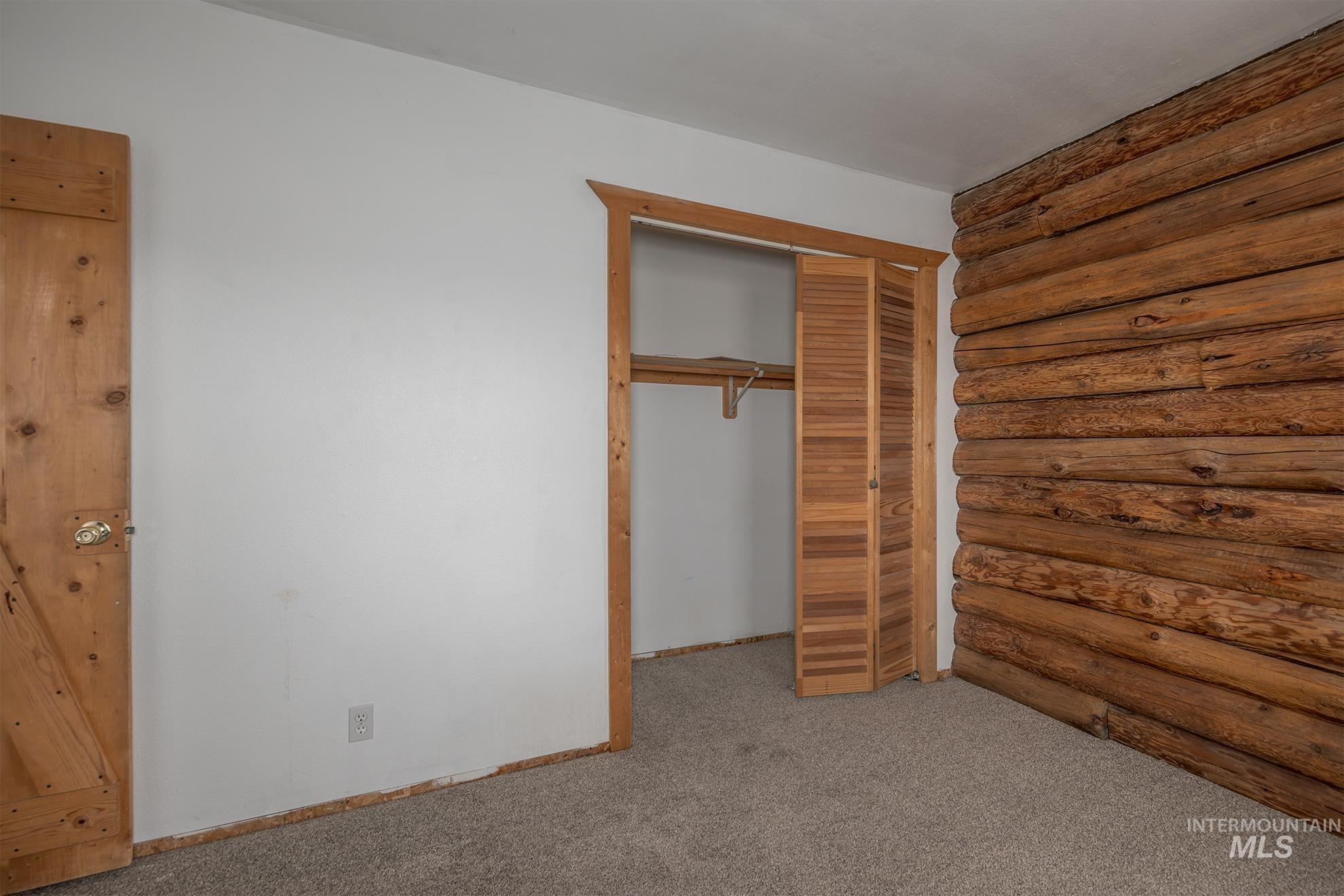 Unfurnished bedroom with log walls, carpet floors, and a closet