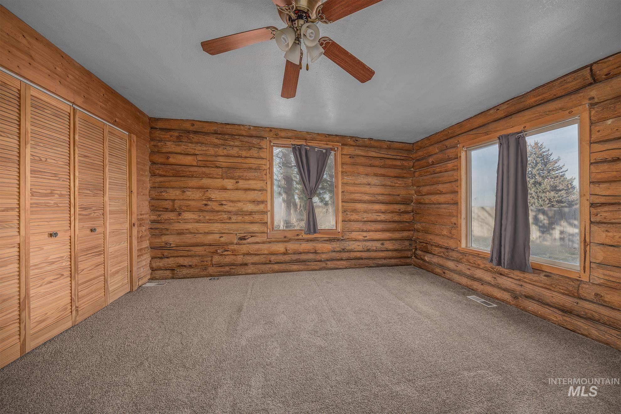 Unfurnished bedroom featuring a closet, carpet floors, ceiling fan, and log walls