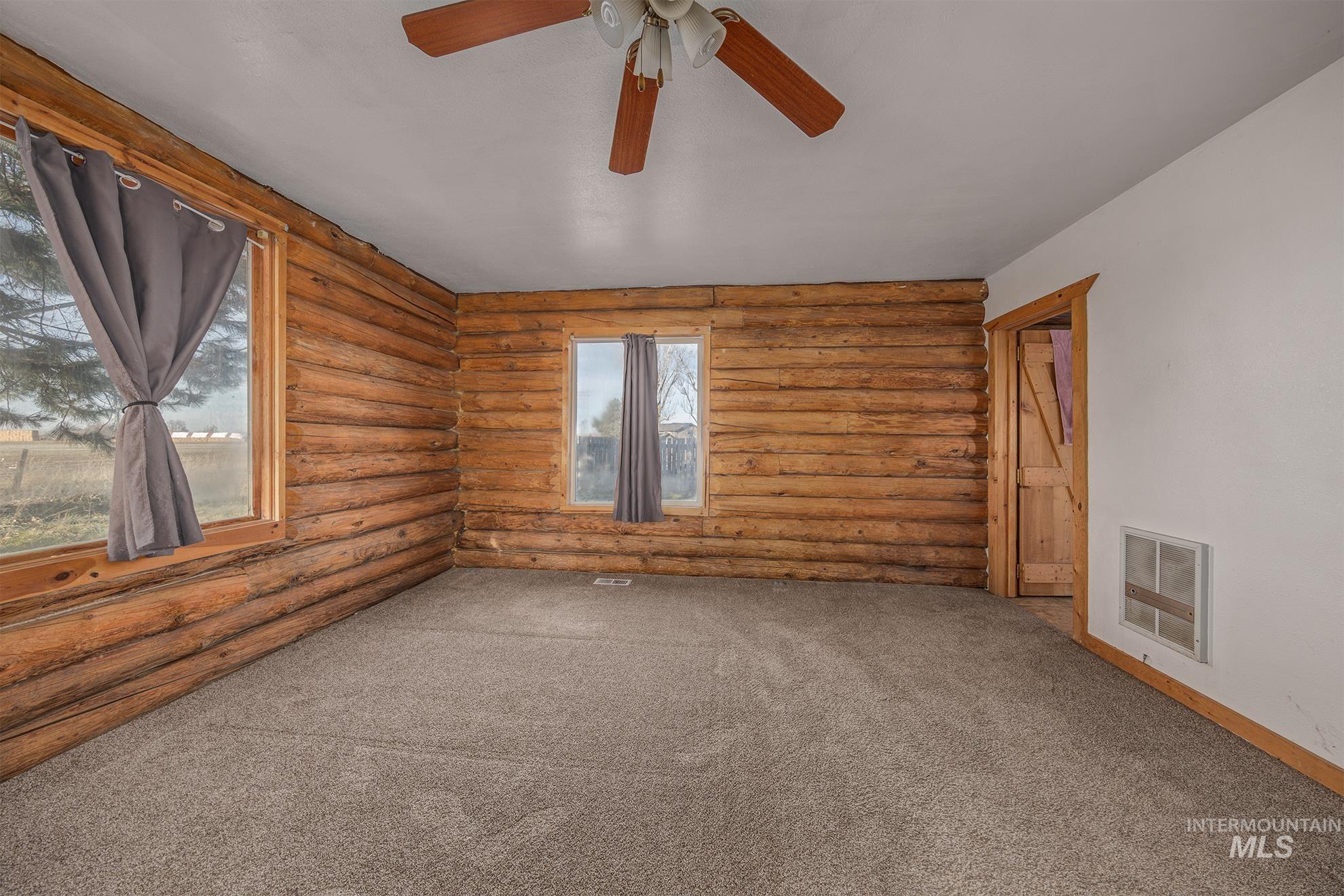 Empty room with rustic walls, carpet floors, and ceiling fan