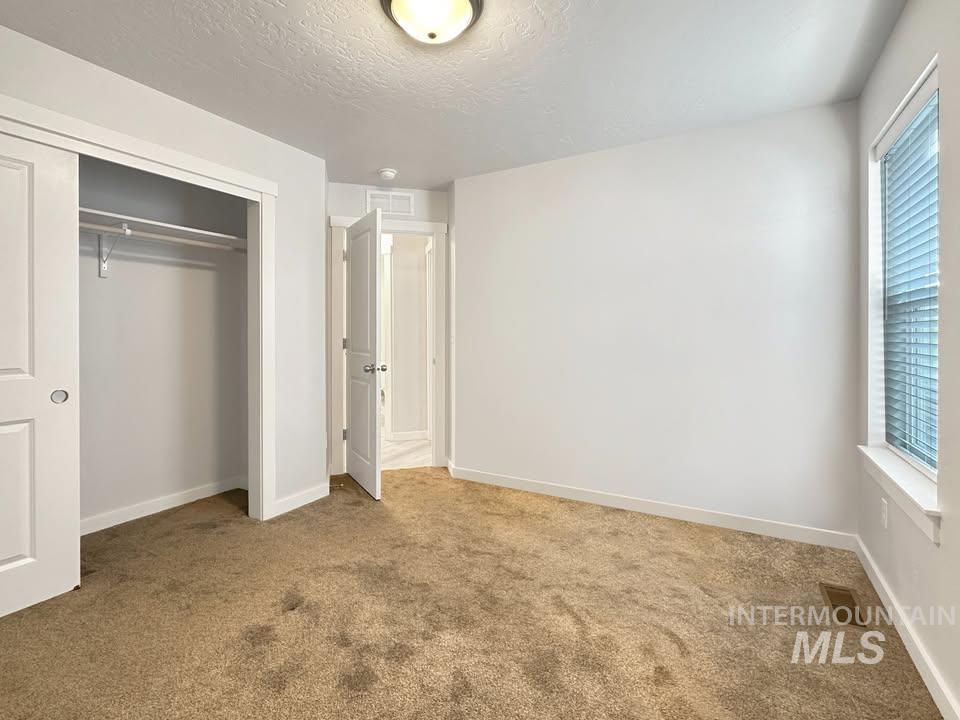 Unfurnished bedroom with carpet, a closet, a textured ceiling, and multiple windows