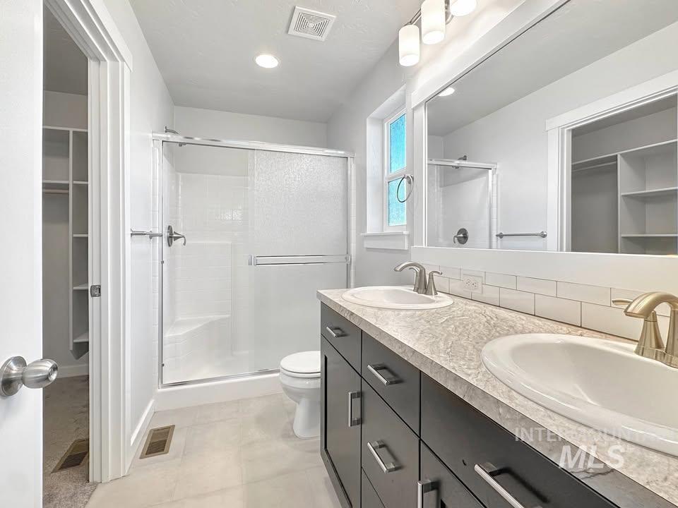 Full bathroom featuring a spacious closet, double vanity, a stall shower, and tasteful backsplash