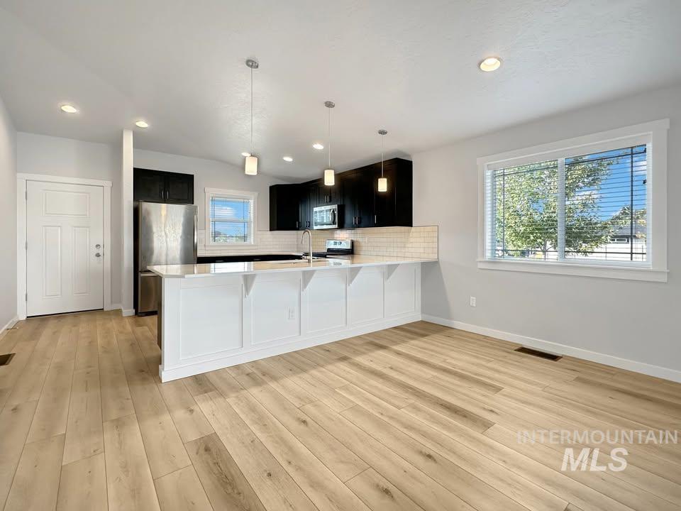 Kitchen with dark cabinets, appliances with stainless steel finishes, decorative light fixtures, a peninsula, and recessed lighting
