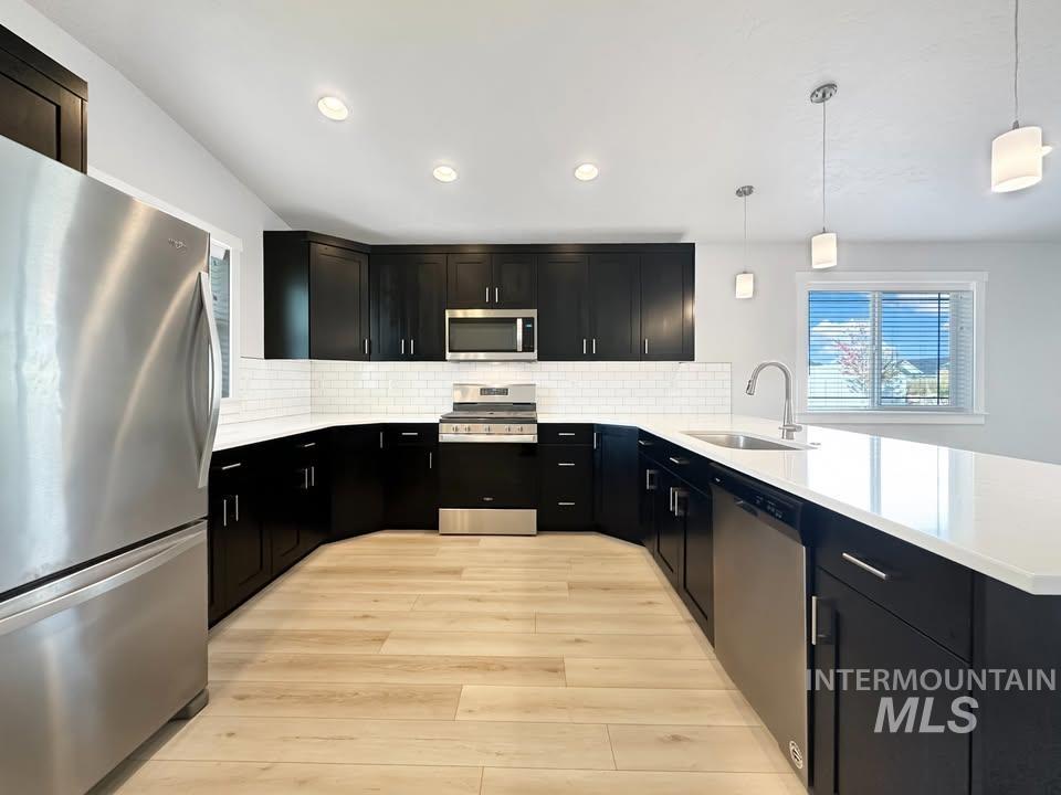 Kitchen featuring dark cabinetry, stainless steel appliances, decorative light fixtures, light stone counters, and recessed lighting