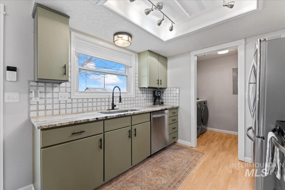 Kitchen with a textured ceiling, green cabinets, backsplash, light stone counters, and stainless steel appliances