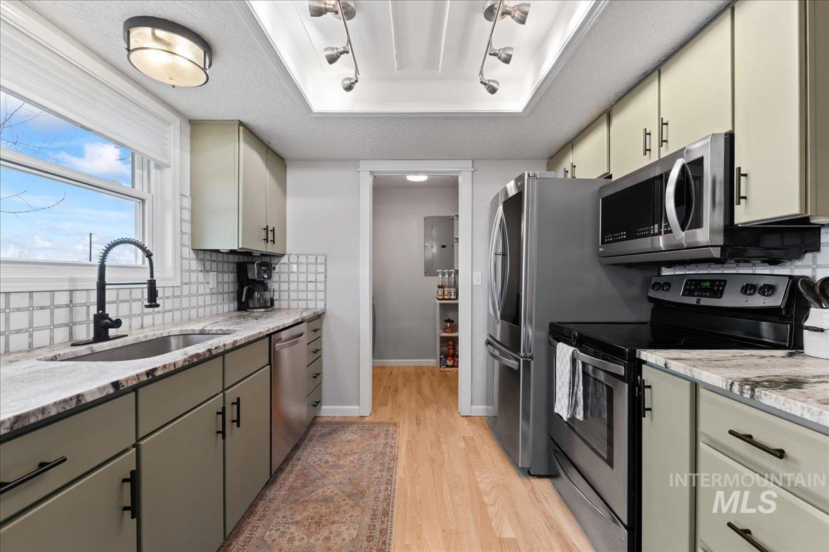 Kitchen with appliances with stainless steel finishes, decorative backsplash, light stone counters, and a textured ceiling