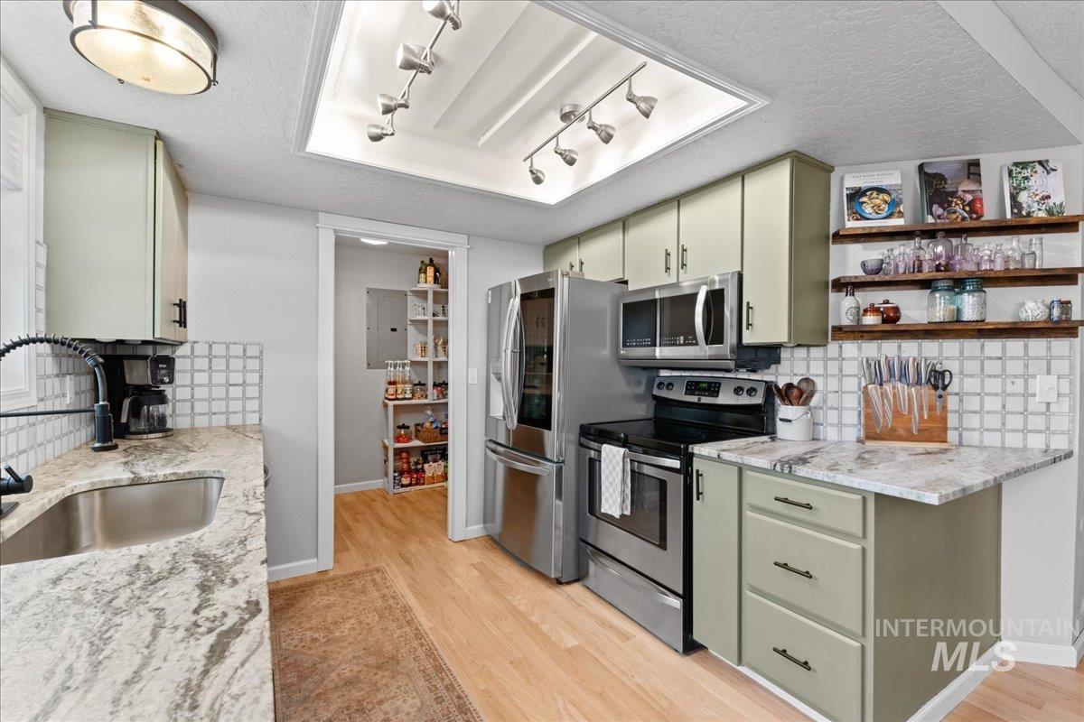 Kitchen with decorative backsplash, green cabinetry, stainless steel appliances, light stone countertops, and a textured ceiling