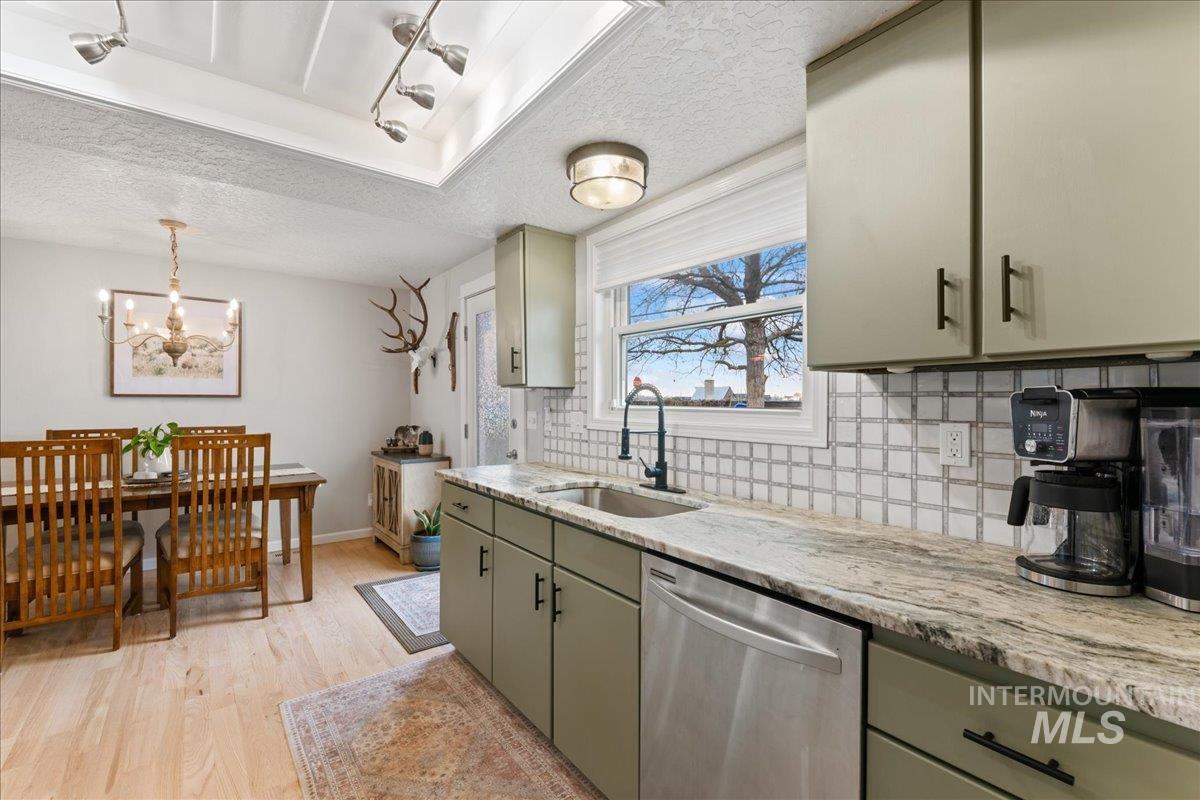 Kitchen featuring a textured ceiling, stainless steel dishwasher, light stone countertops, tasteful backsplash, and light wood-type flooring