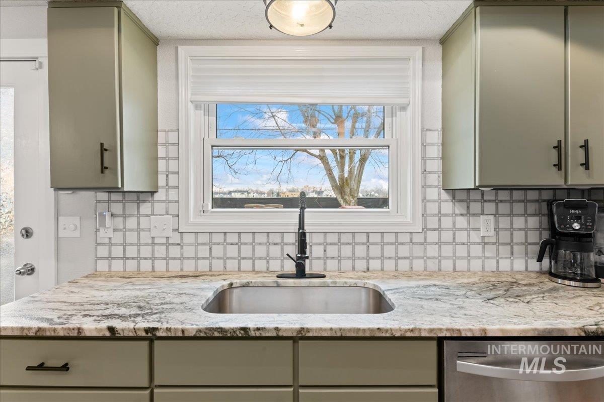 Kitchen featuring stainless steel dishwasher, light stone counters, tasteful backsplash, and gray cabinetry