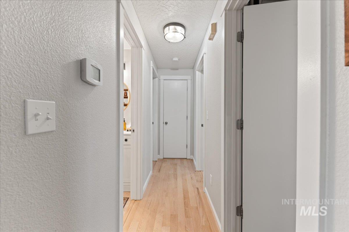 Hallway with a textured wall, light wood-style floors, and a textured ceiling
