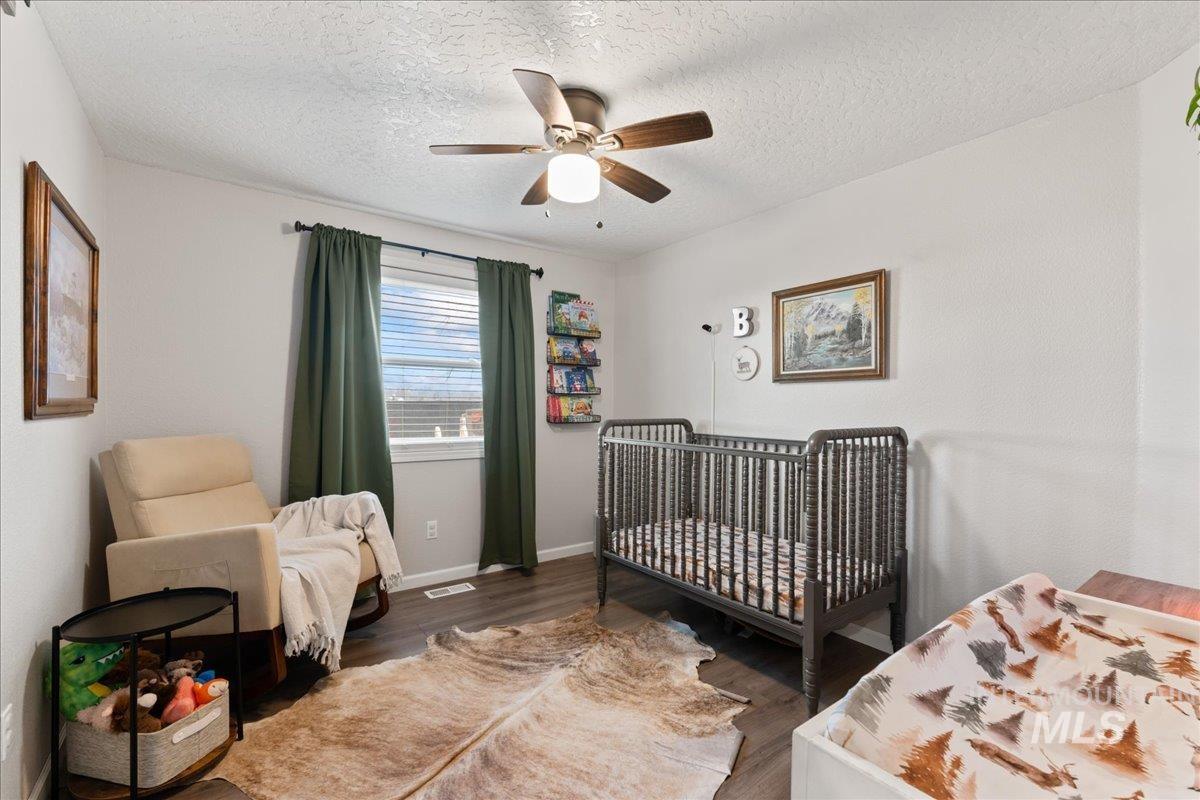 Bedroom with a crib, a ceiling fan, wood finished floors, and a textured ceiling