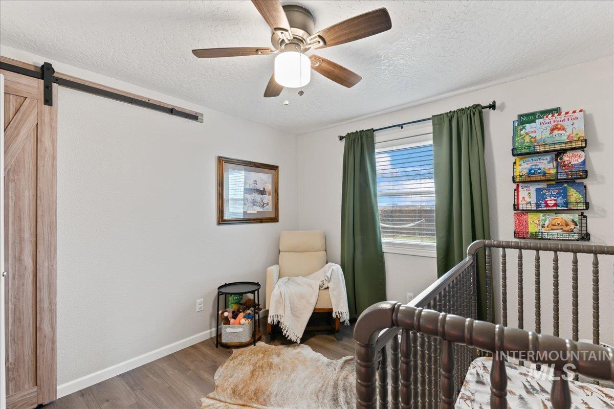 Bedroom featuring a barn door, wood finished floors, a textured ceiling, a ceiling fan, and a crib
