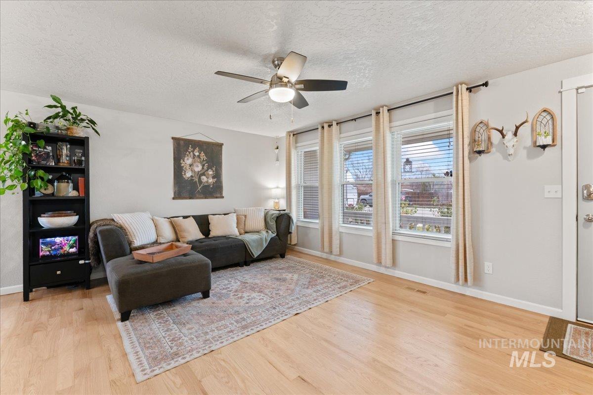 Living room featuring a textured ceiling, a ceiling fan, and light wood-style flooring