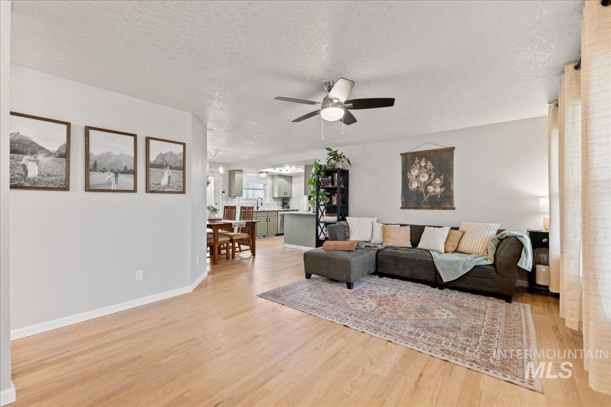 Living area with a textured ceiling, a ceiling fan, and light wood-style floors