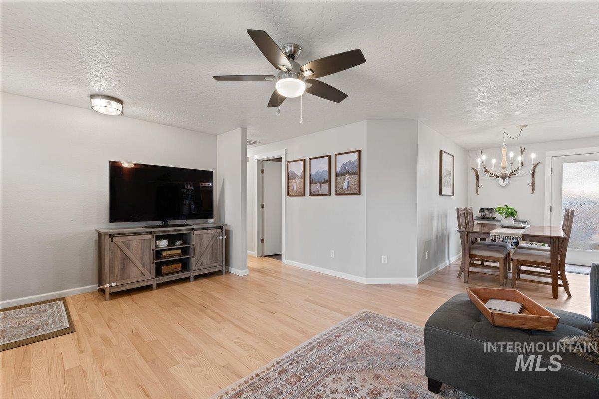 Living room with a textured ceiling, light wood-style flooring, ceiling fan, and a chandelier