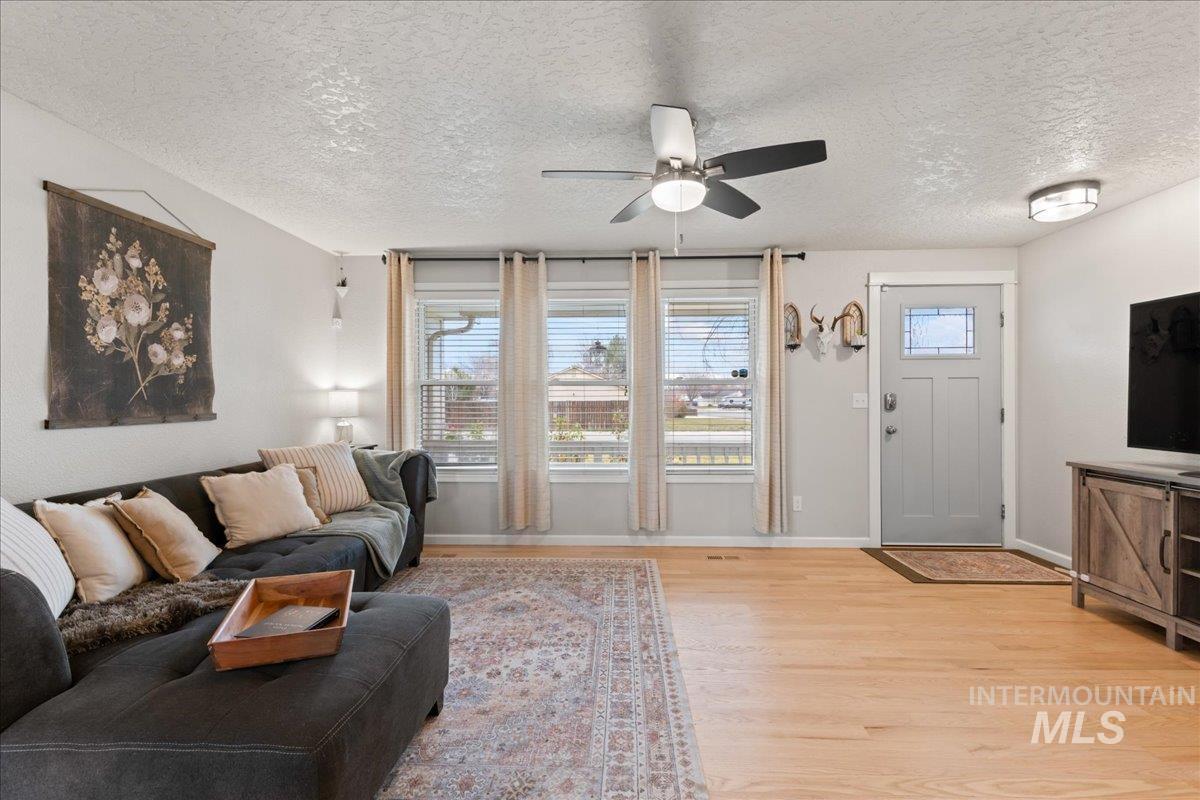 Living room featuring plenty of natural light, a textured ceiling, a ceiling fan, and light wood-style flooring