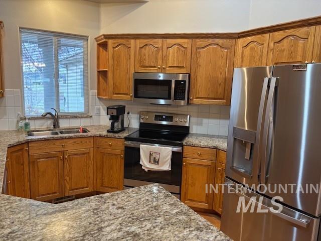 Kitchen with appliances with stainless steel finishes, brown cabinetry, light stone counters, and decorative backsplash