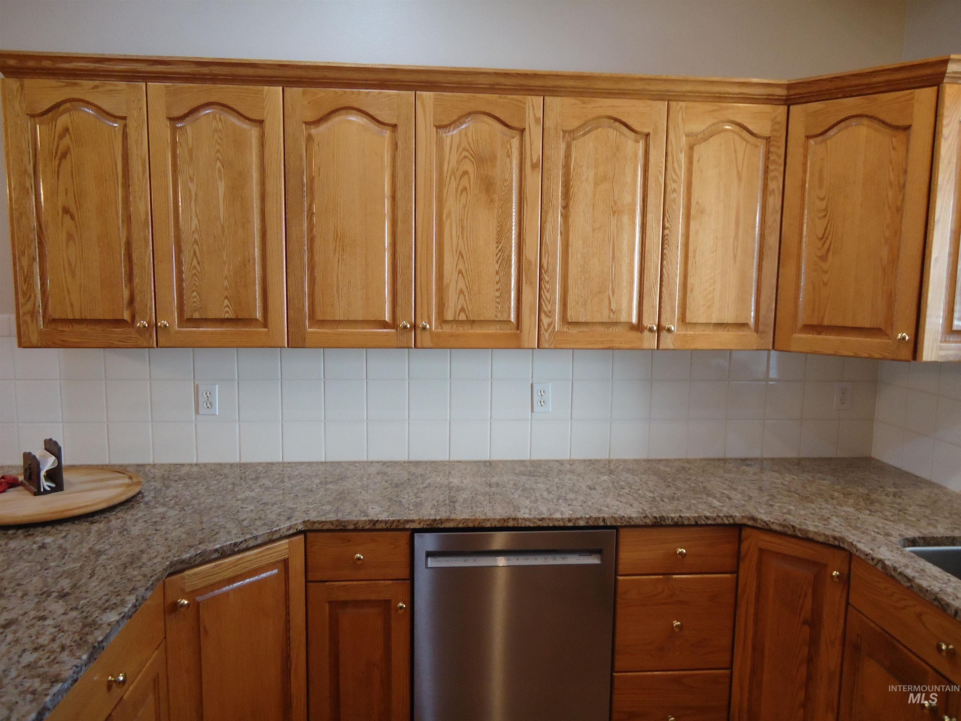 Kitchen featuring dark stone counters, dishwasher, backsplash, and brown cabinets