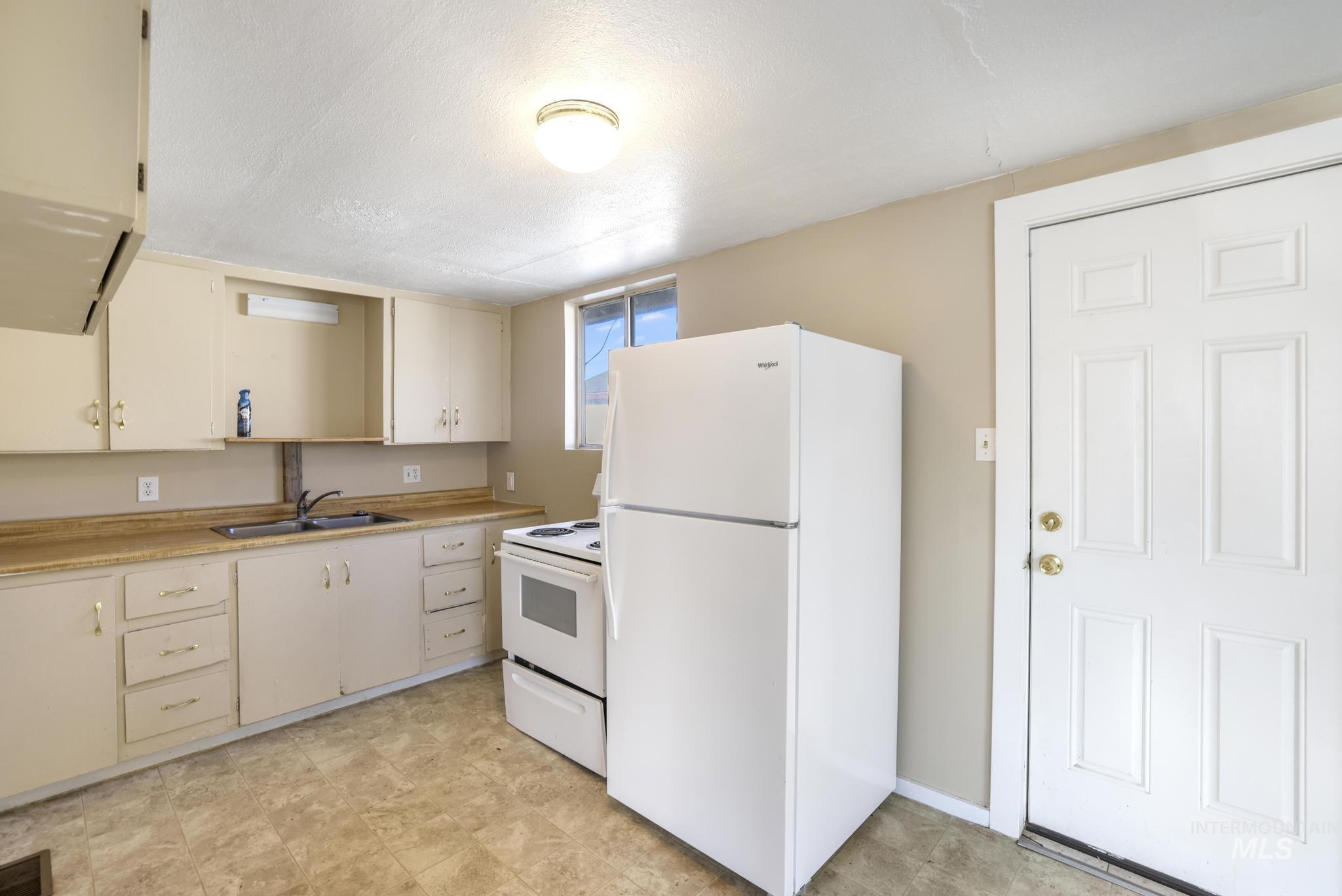 Kitchen with white appliances, light countertops, open shelves, a textured ceiling, and cream cabinetry
