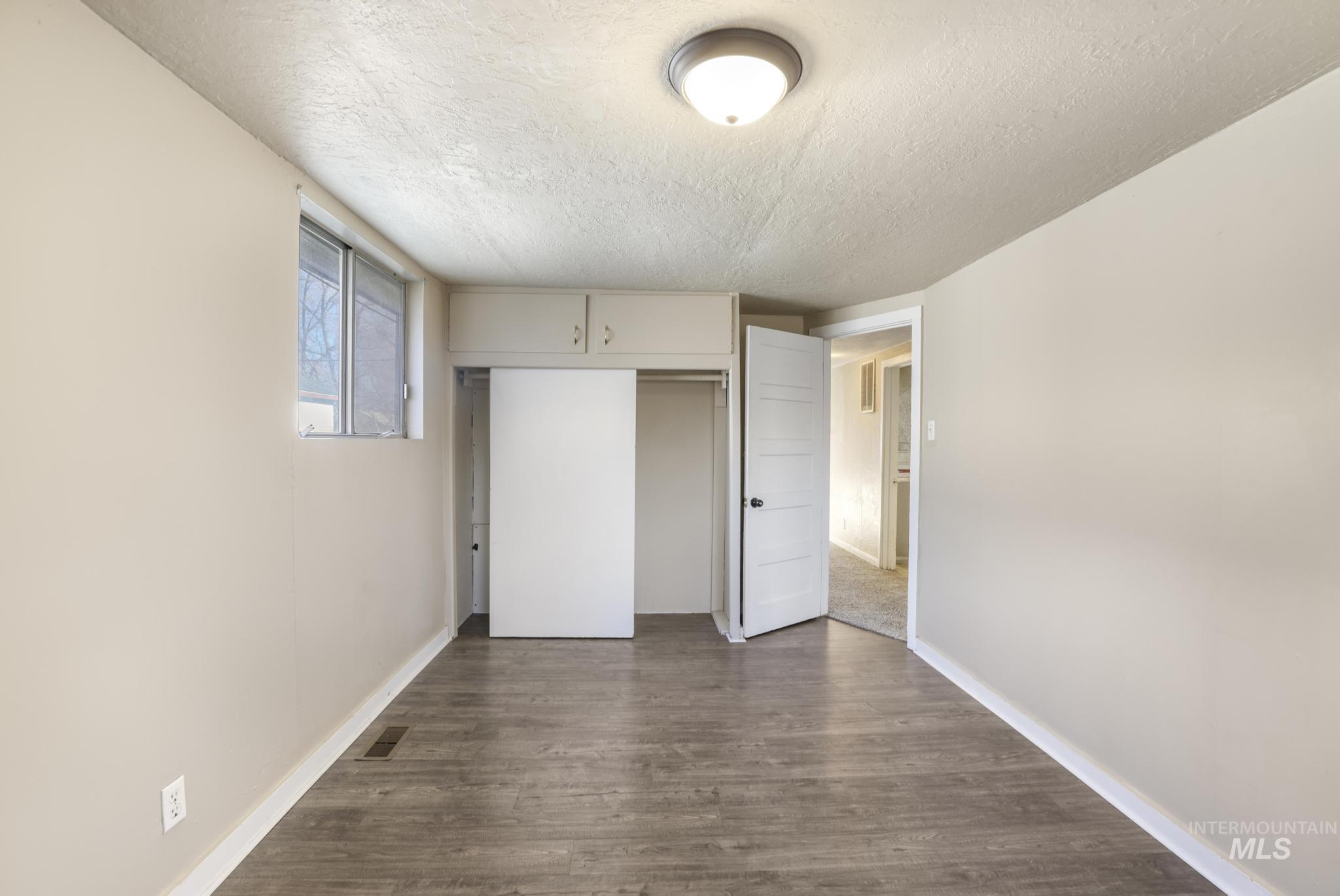 Unfurnished bedroom featuring a textured ceiling, dark wood-style floors, and a closet