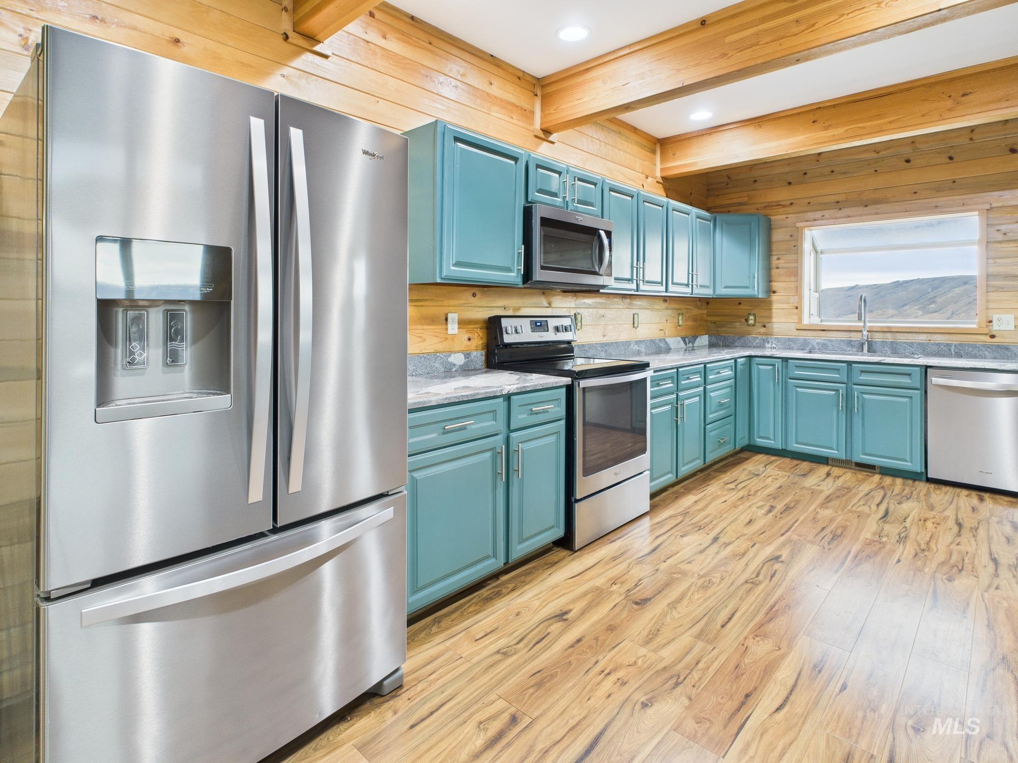 Kitchen featuring appliances with stainless steel finishes, wood walls, light wood finished floors, beamed ceiling, and blue cabinets
