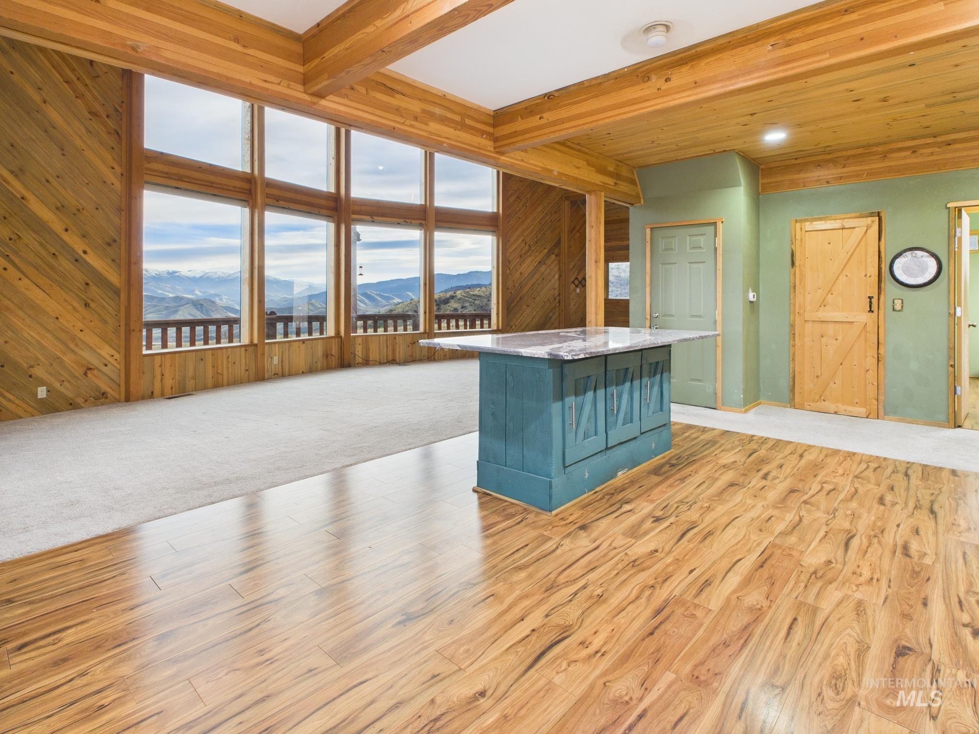 Kitchen with beamed ceiling, a mountain view, wooden walls, light wood-type flooring, and light stone countertops