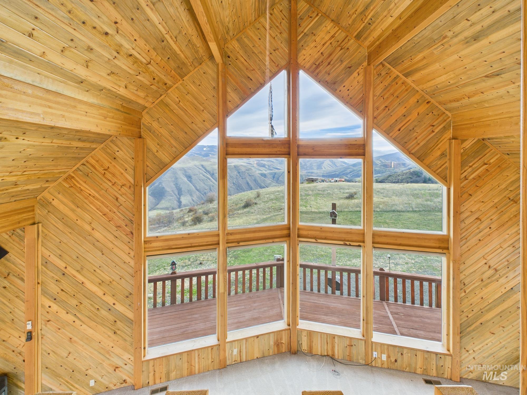 Unfurnished living room with wooden ceiling, wooden walls, healthy amount of natural light, a mountain view, and light carpet