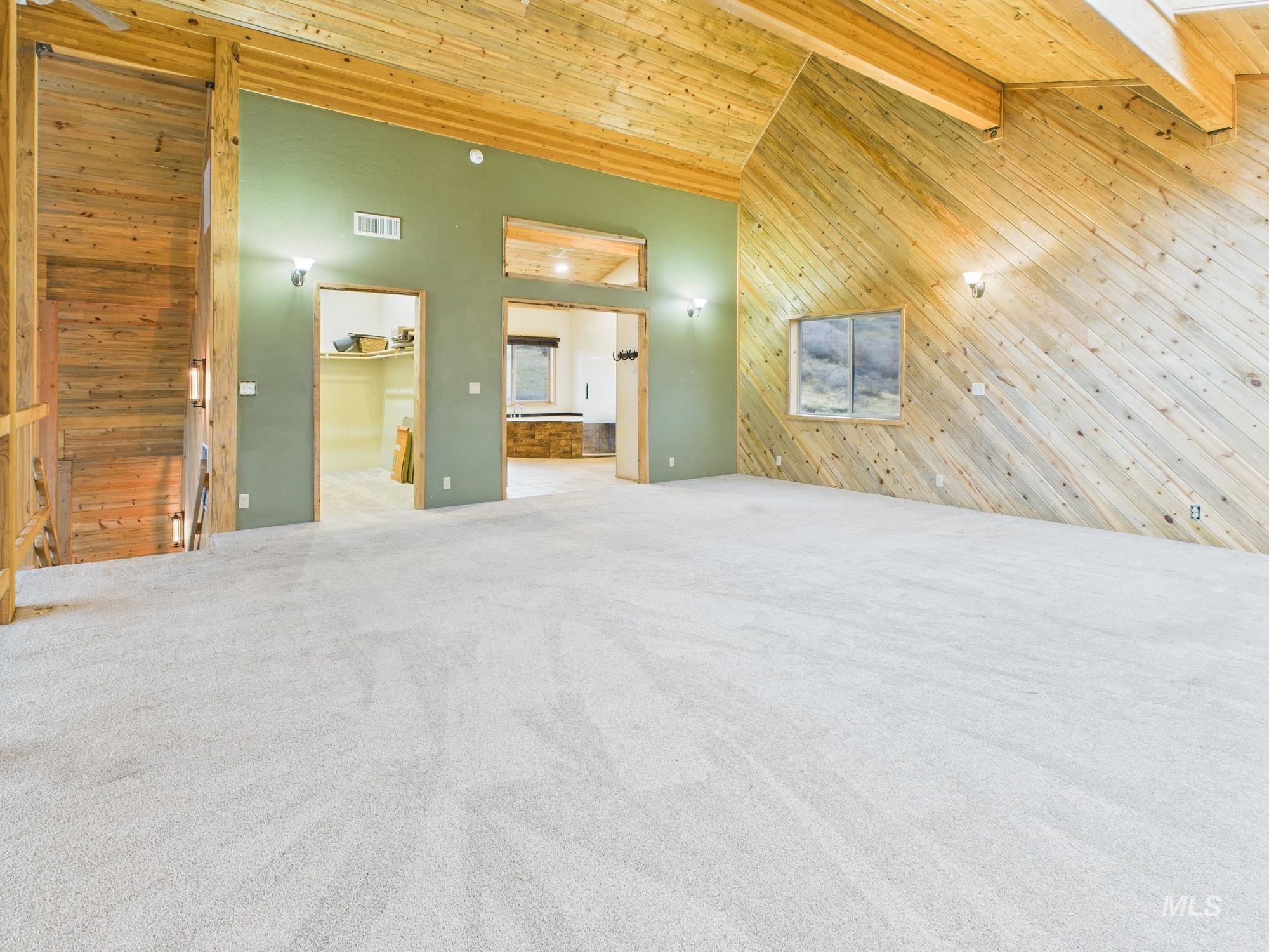 Master bedroom with wooden walls, high vaulted ceiling, connected bathroom, light carpet, and a wooden ceiling with exposed beams