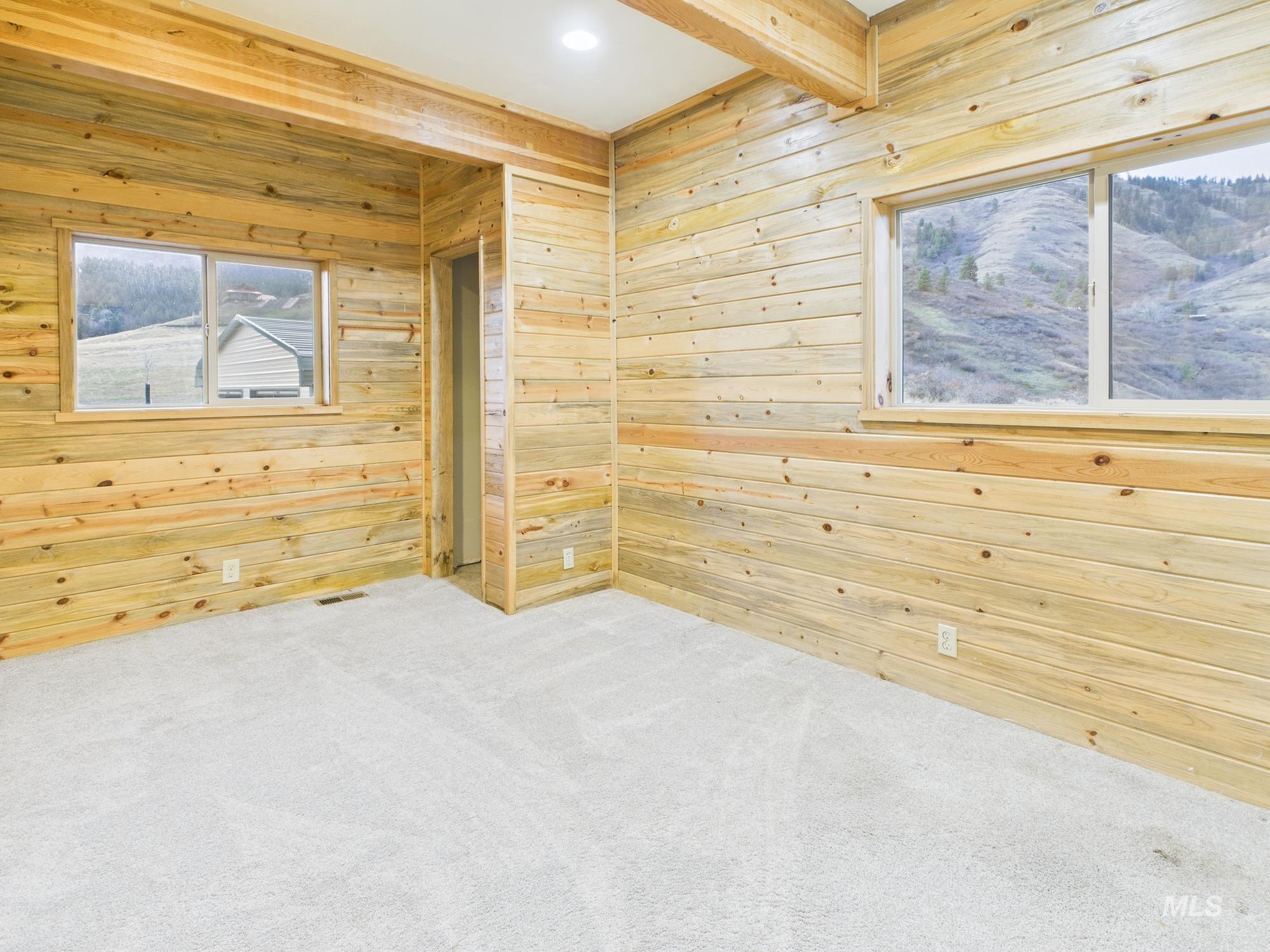 Spare room with wood walls, light carpet, and beamed ceiling