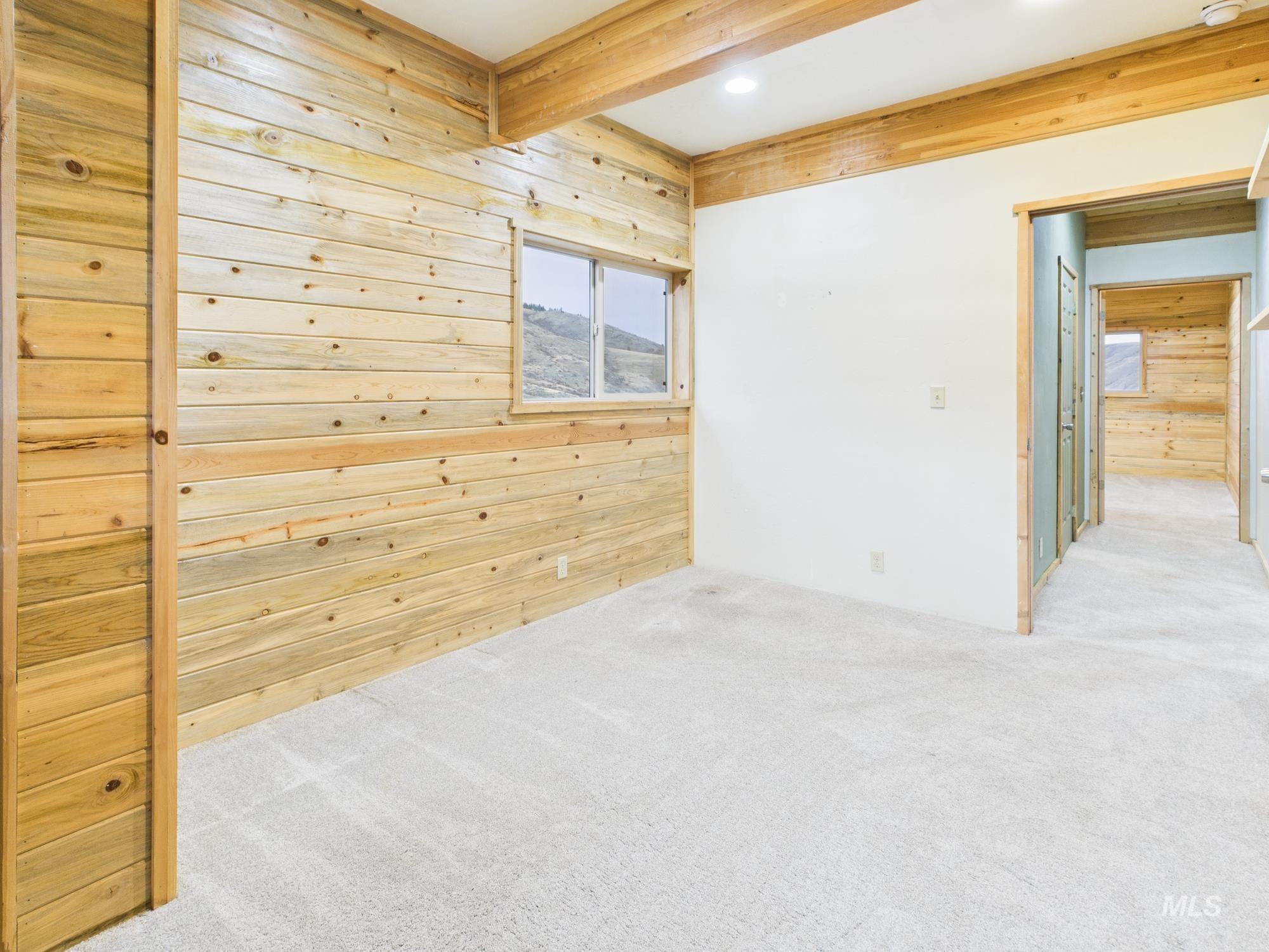 Spare room with wooden walls, light carpet, beam ceiling, and recessed lighting