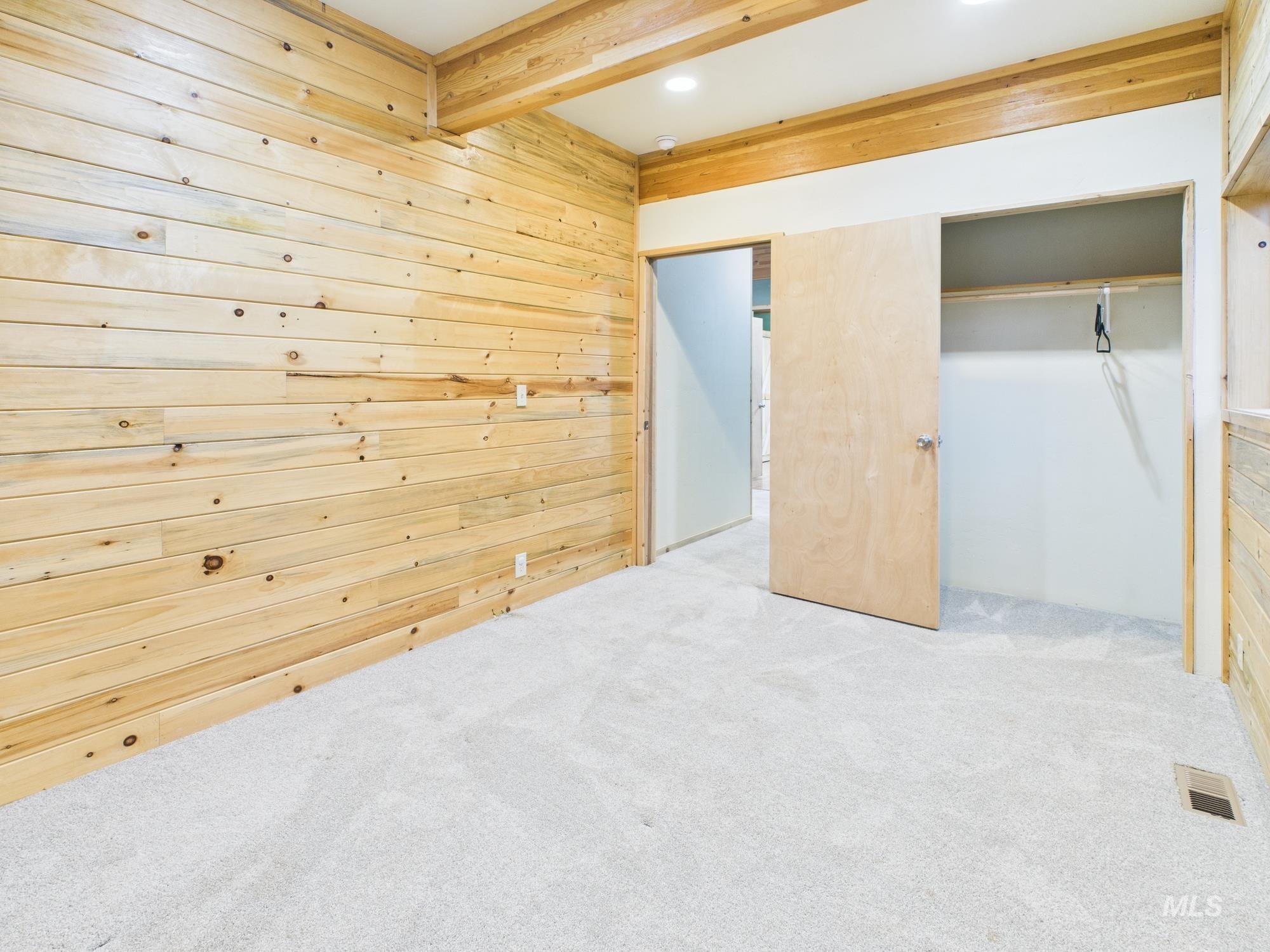 Unfurnished bedroom featuring wood walls, carpet flooring, beamed ceiling, and recessed lighting