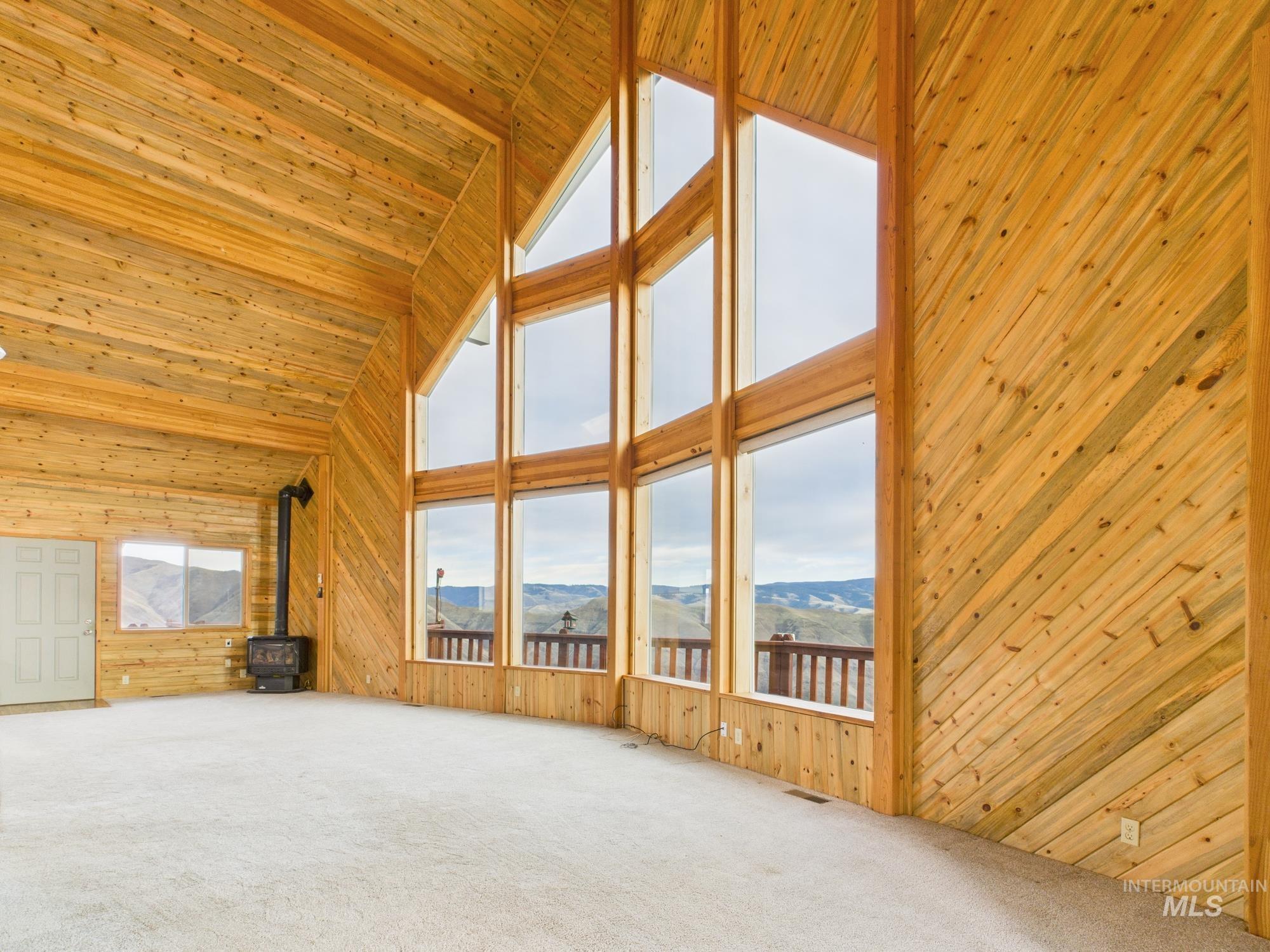 Unfurnished living room featuring wooden walls, high vaulted ceiling, a wood stove, carpet, and wooden ceiling