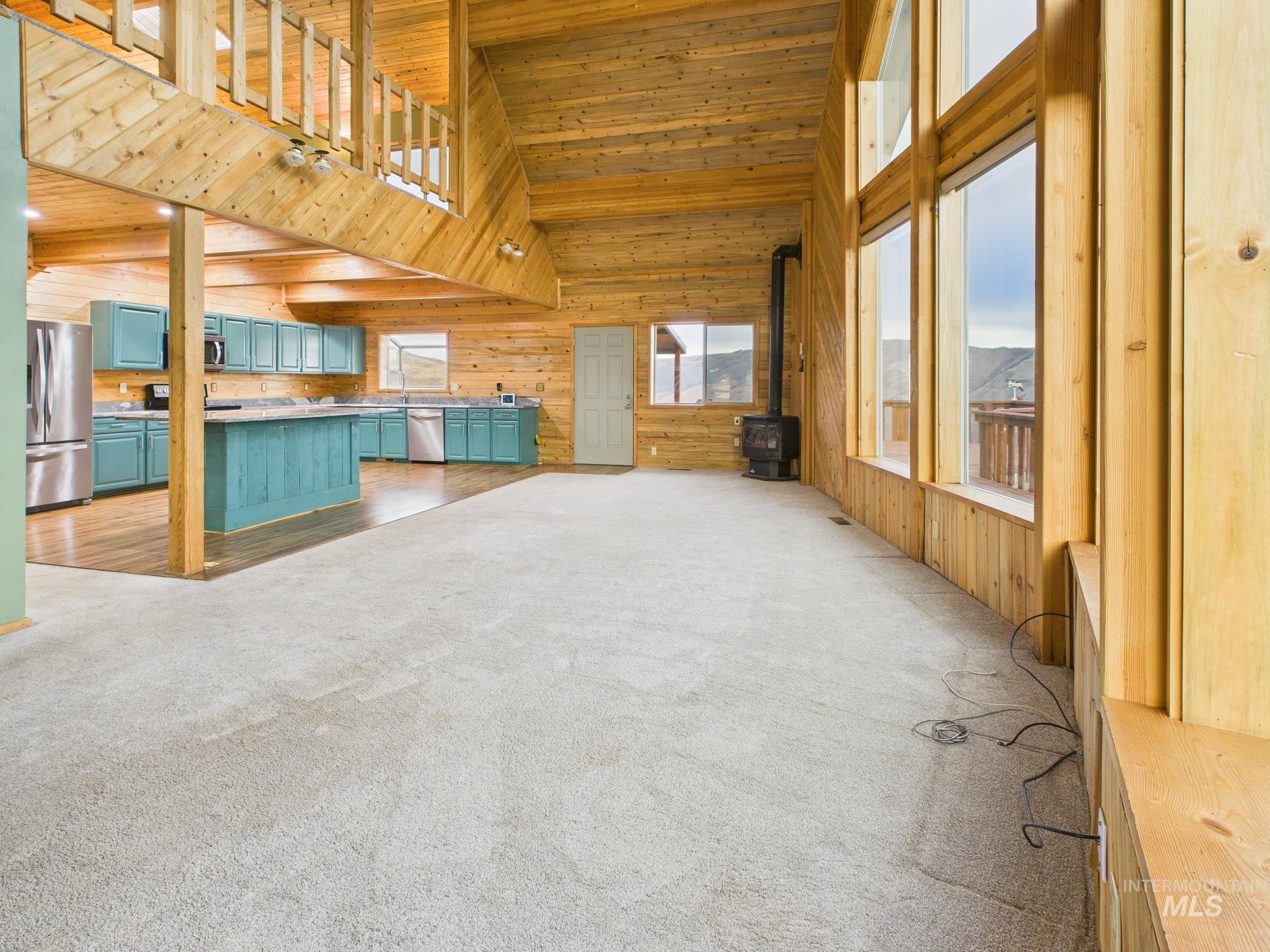 Unfurnished living room featuring wooden walls, a wood stove, high vaulted ceiling, wood ceiling, and light carpet