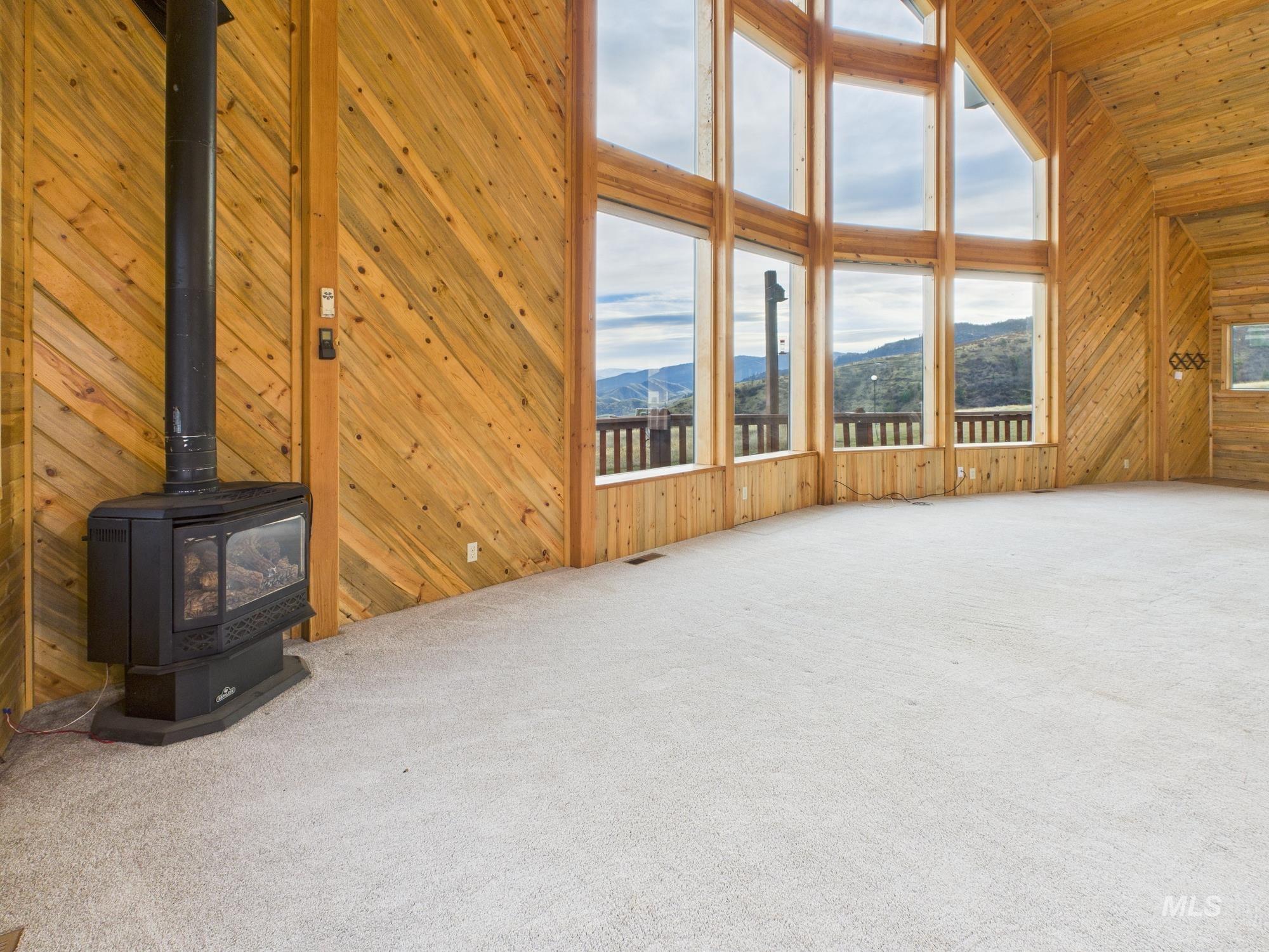 Unfurnished living room with wooden walls, high vaulted ceiling, a wood stove, carpet floors, and a mountain view