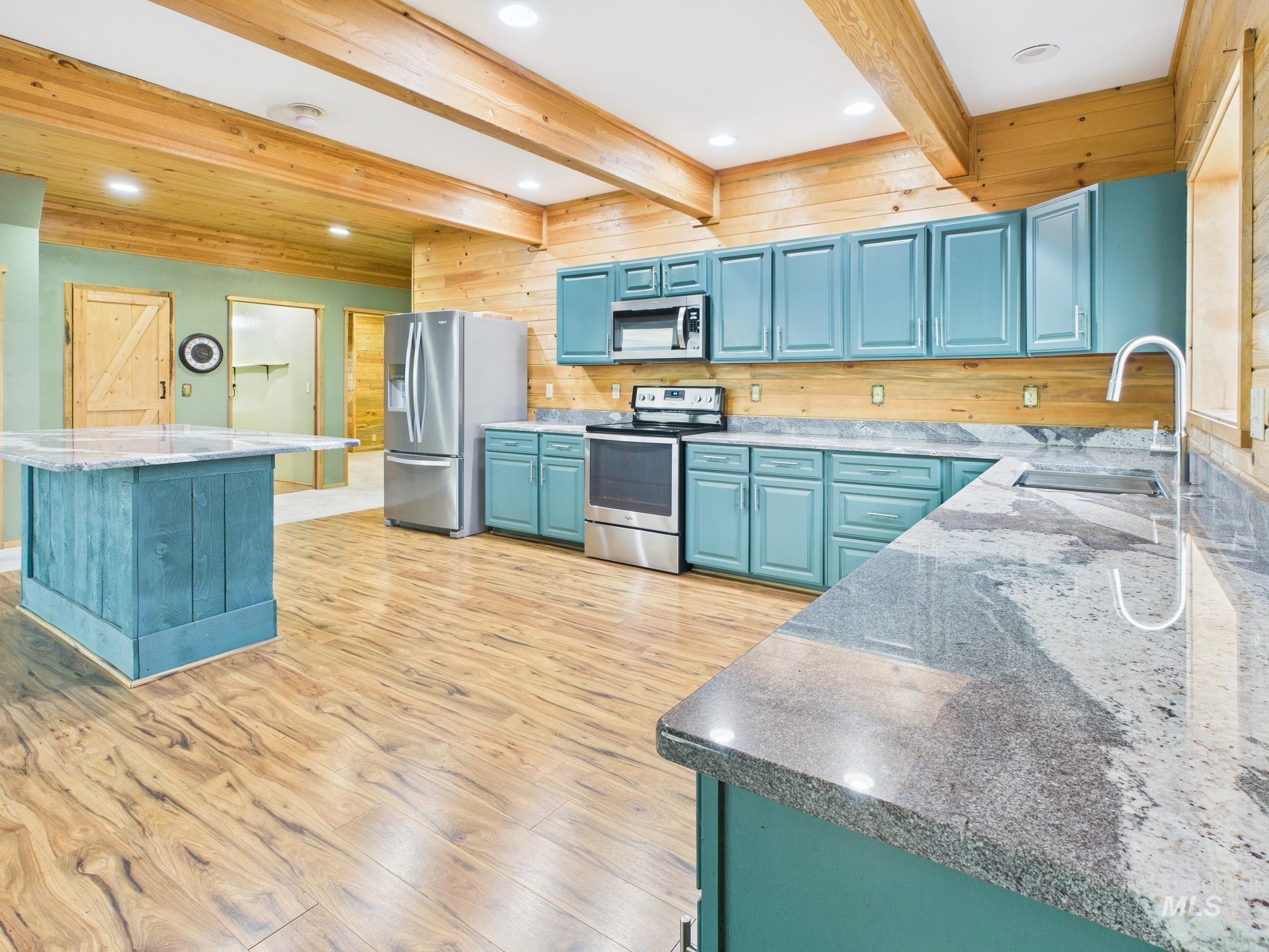 Kitchen with blue cabinetry, stainless steel appliances, beam ceiling, light wood-style floors, and light stone counters