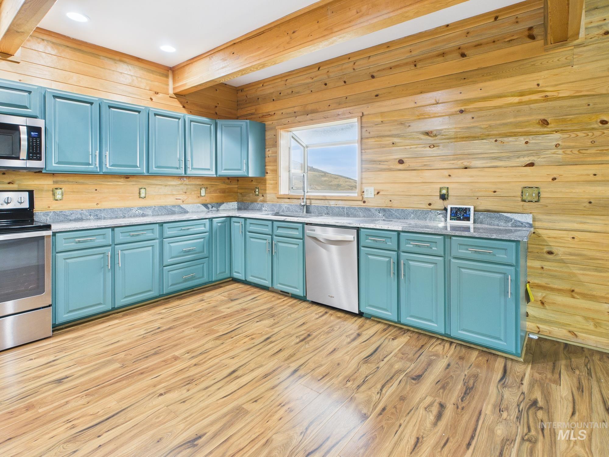 Kitchen featuring wooden walls, blue cabinets, stainless steel appliances, beam ceiling, and light wood-style flooring