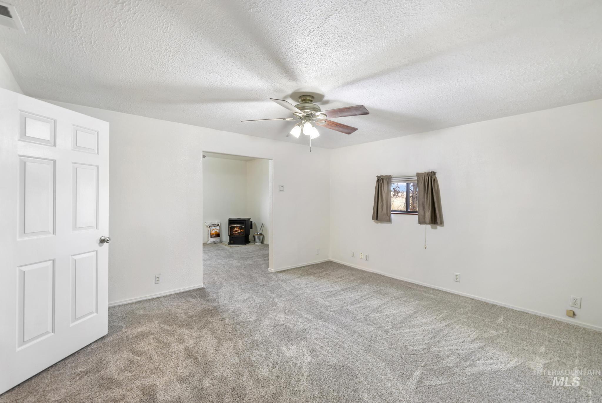 Carpeted spare room featuring a wood stove, a textured ceiling, and a ceiling fan