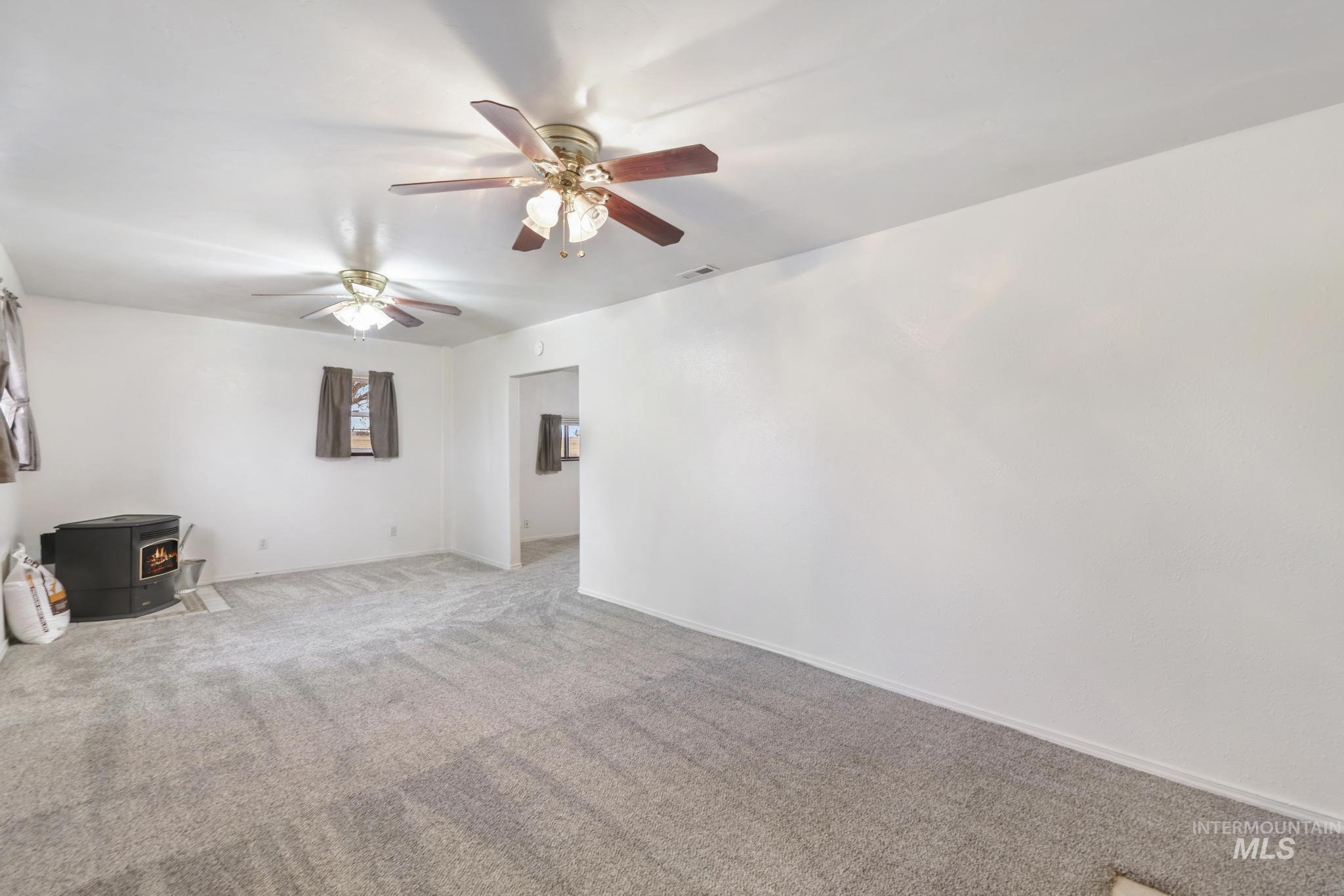 Unfurnished room featuring a wood stove, carpet flooring, and a ceiling fan