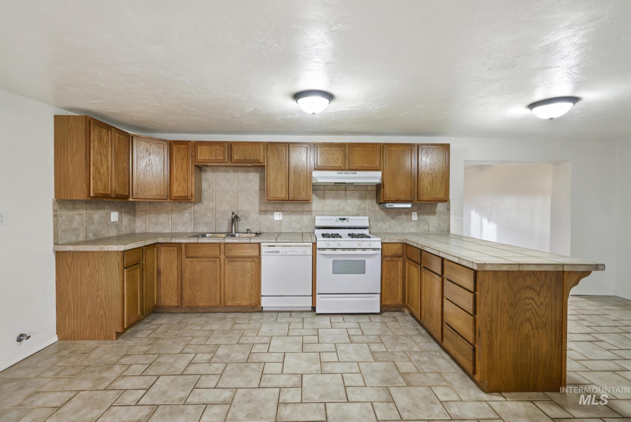 Kitchen with tile countertops, brown cabinets, a peninsula, and white appliances