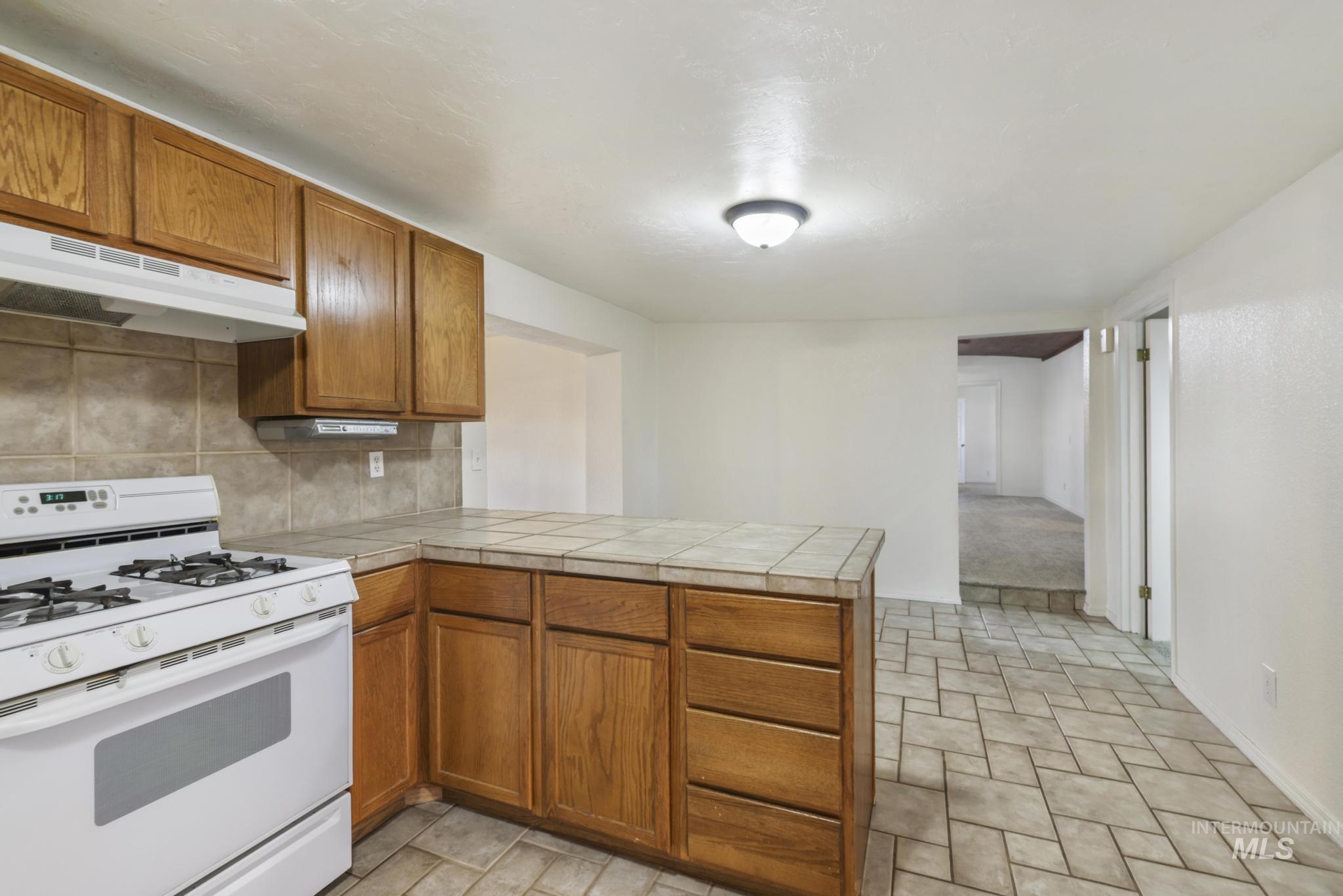 Kitchen featuring white range with gas stovetop, brown cabinetry, backsplash, and a peninsula