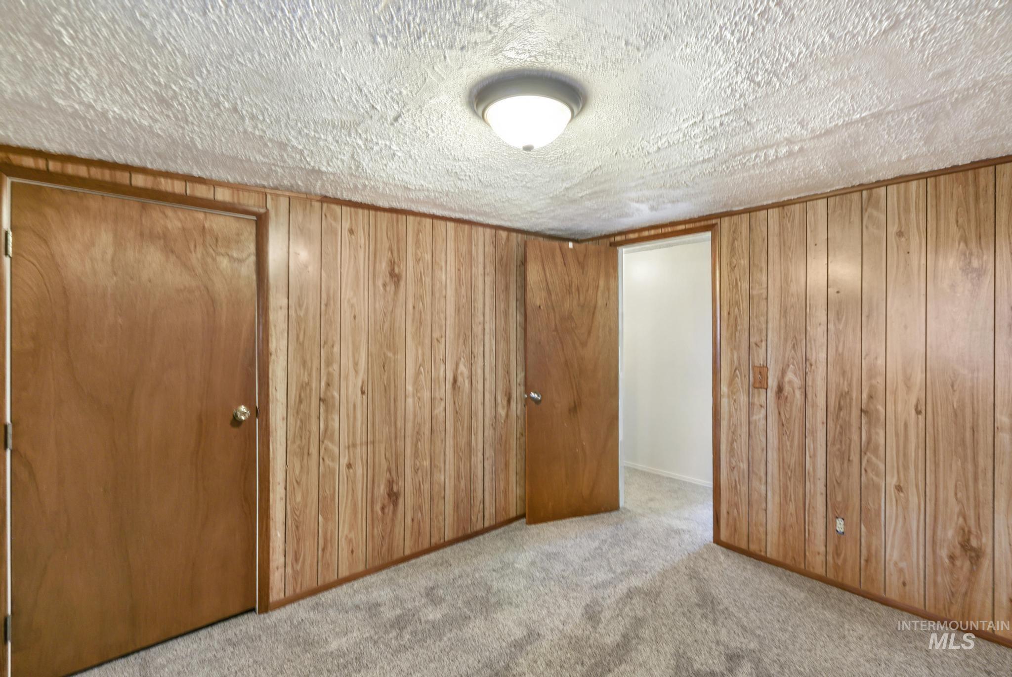 Unfurnished bedroom featuring a closet, light colored carpet, a textured ceiling, and wooden walls