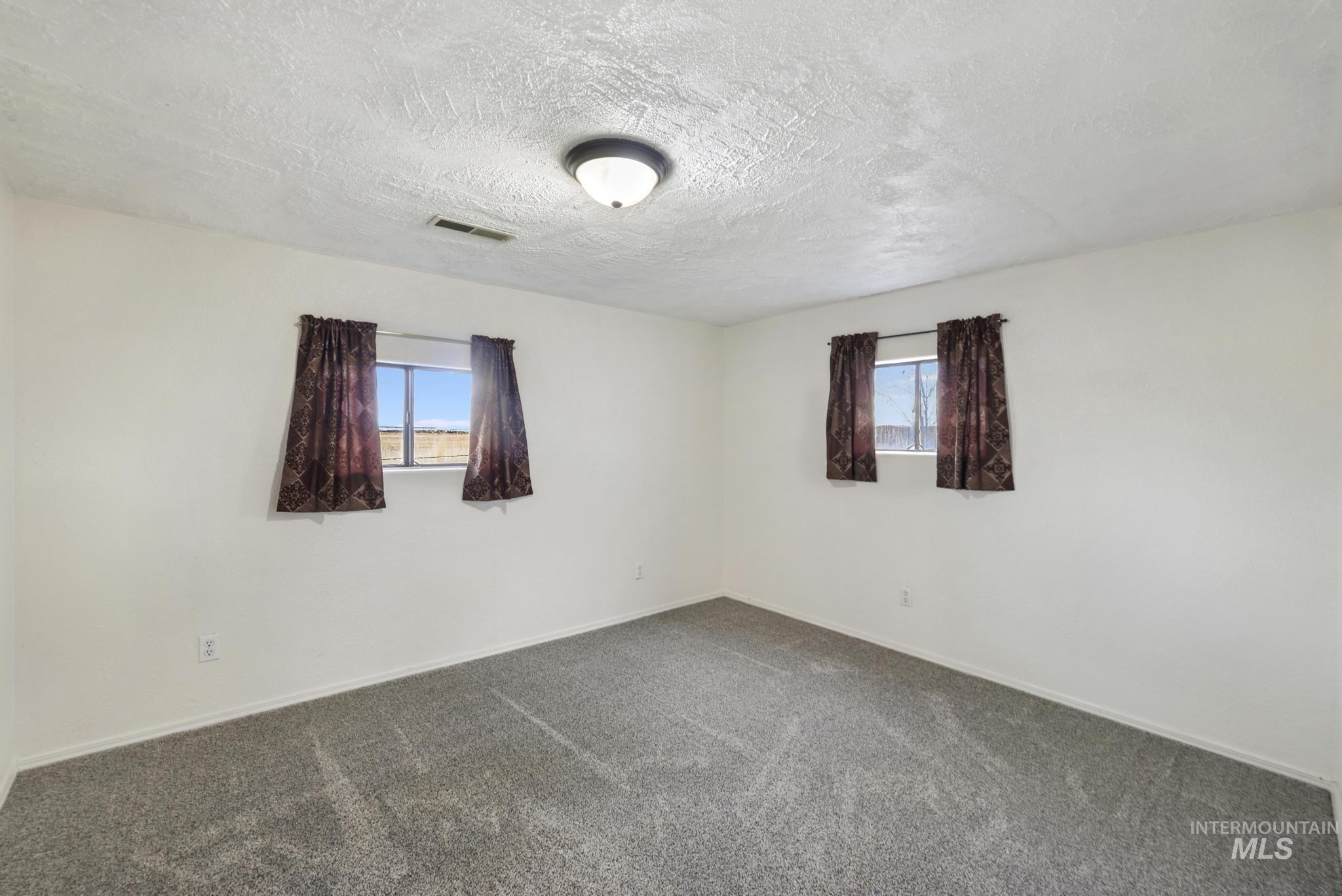 Carpeted empty room featuring a textured ceiling and baseboards
