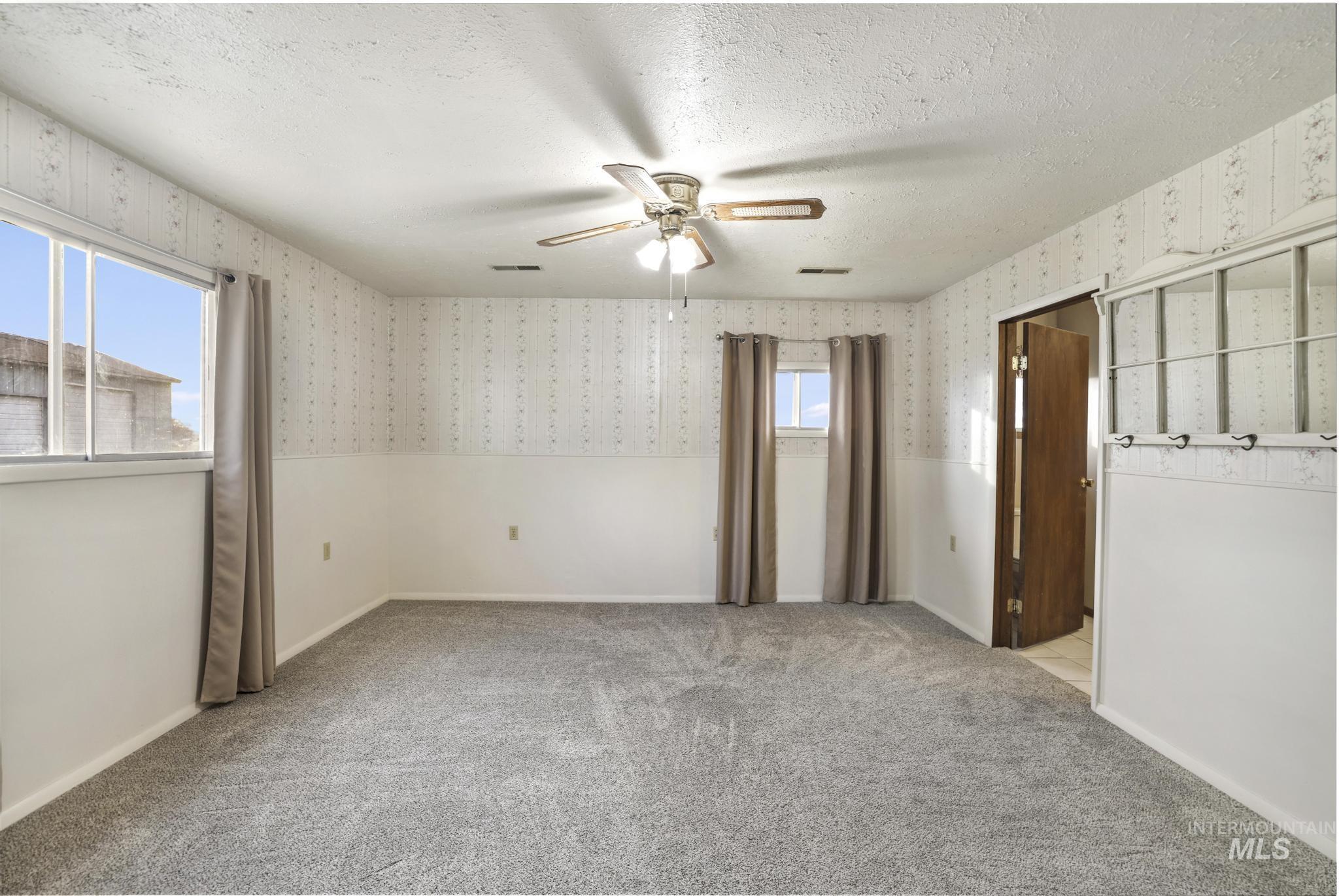 Spare room with a textured ceiling, healthy amount of natural light, light colored carpet, a ceiling fan, and wallpapered walls