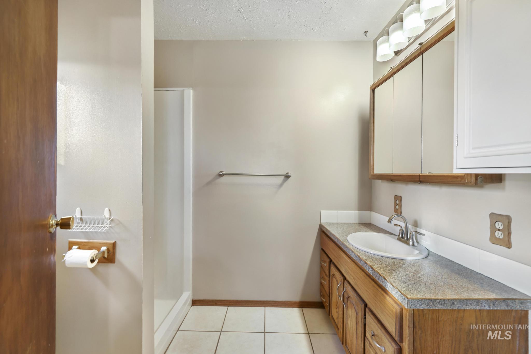Full bathroom featuring vanity, a shower stall, light tile patterned flooring, and a textured ceiling